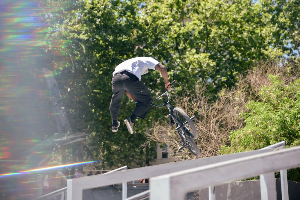 Rider BMX sautant au-dessus d’une rampe, en partie dissimulé par la végétation.