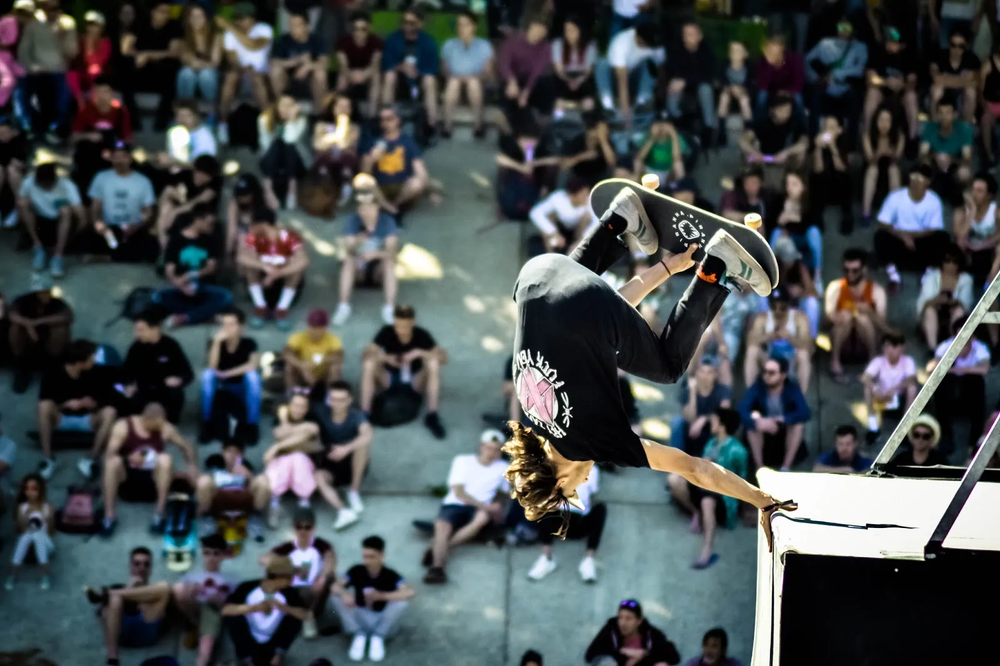 Skateur en plein saut sur une rampe, public en arrière-plan dans les gradins.