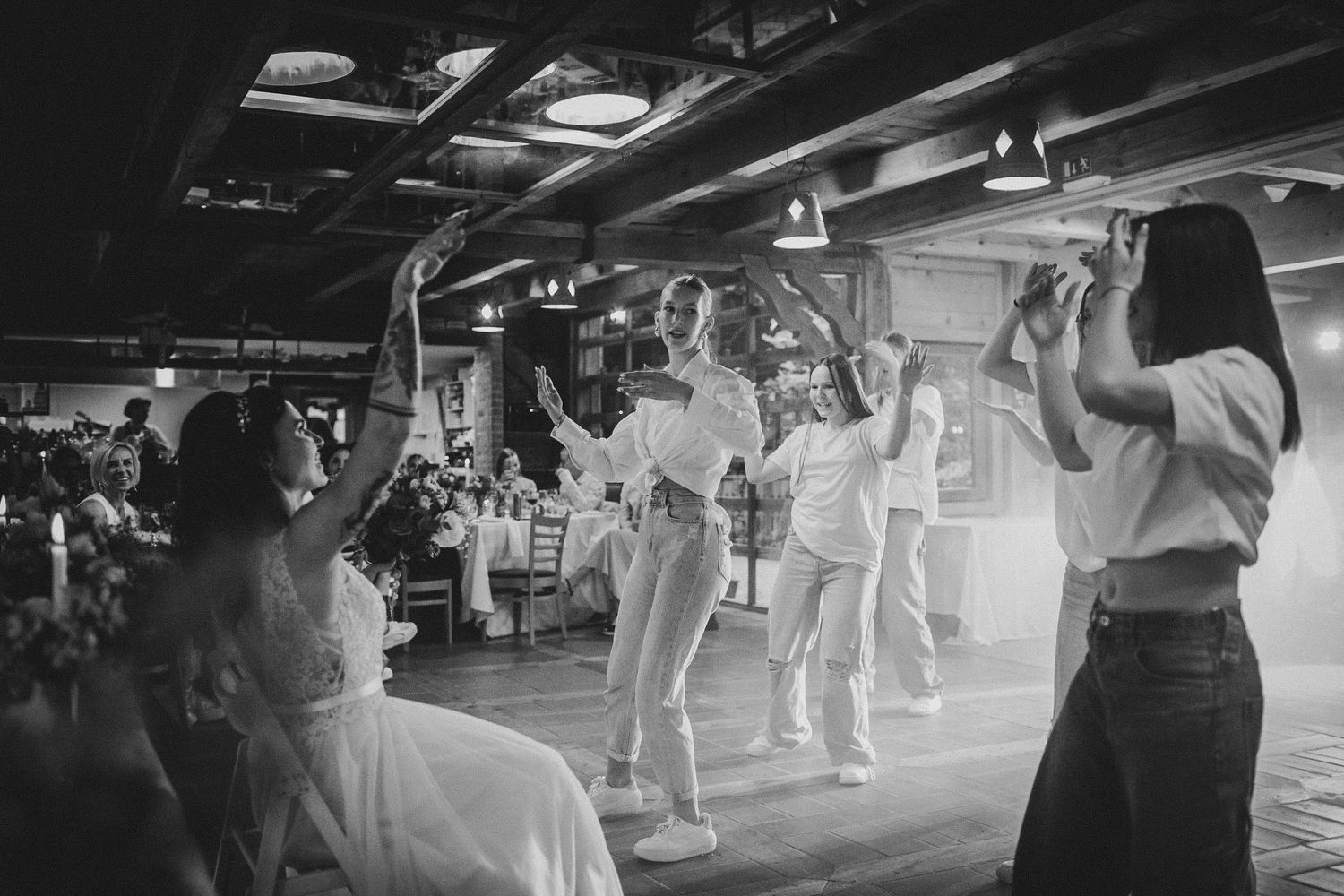 Black and white photo of wedding guests dancing and celebrating in an indoor venue.