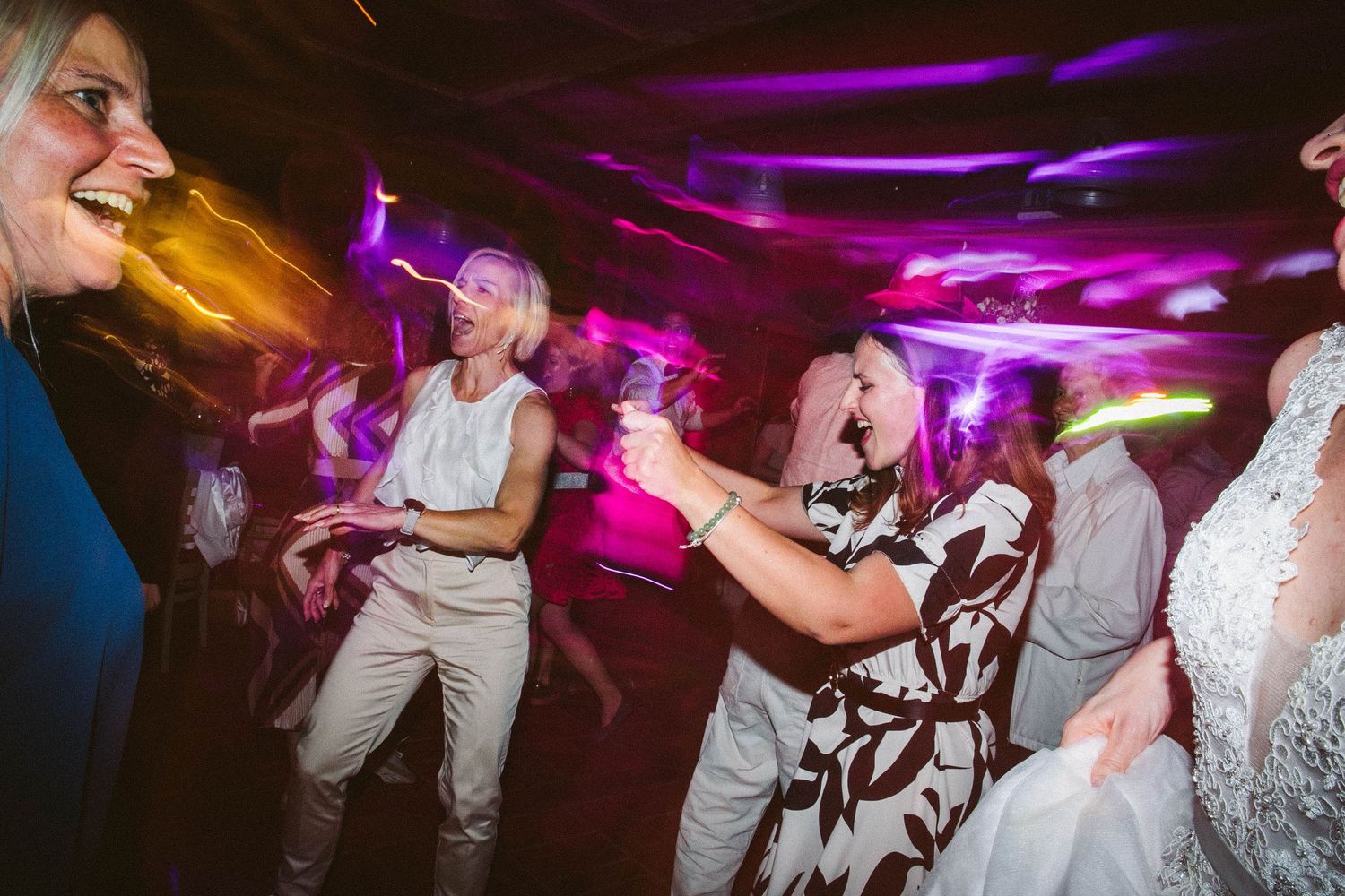 Energetic dancing at wedding reception with colorful purple lighting effects.