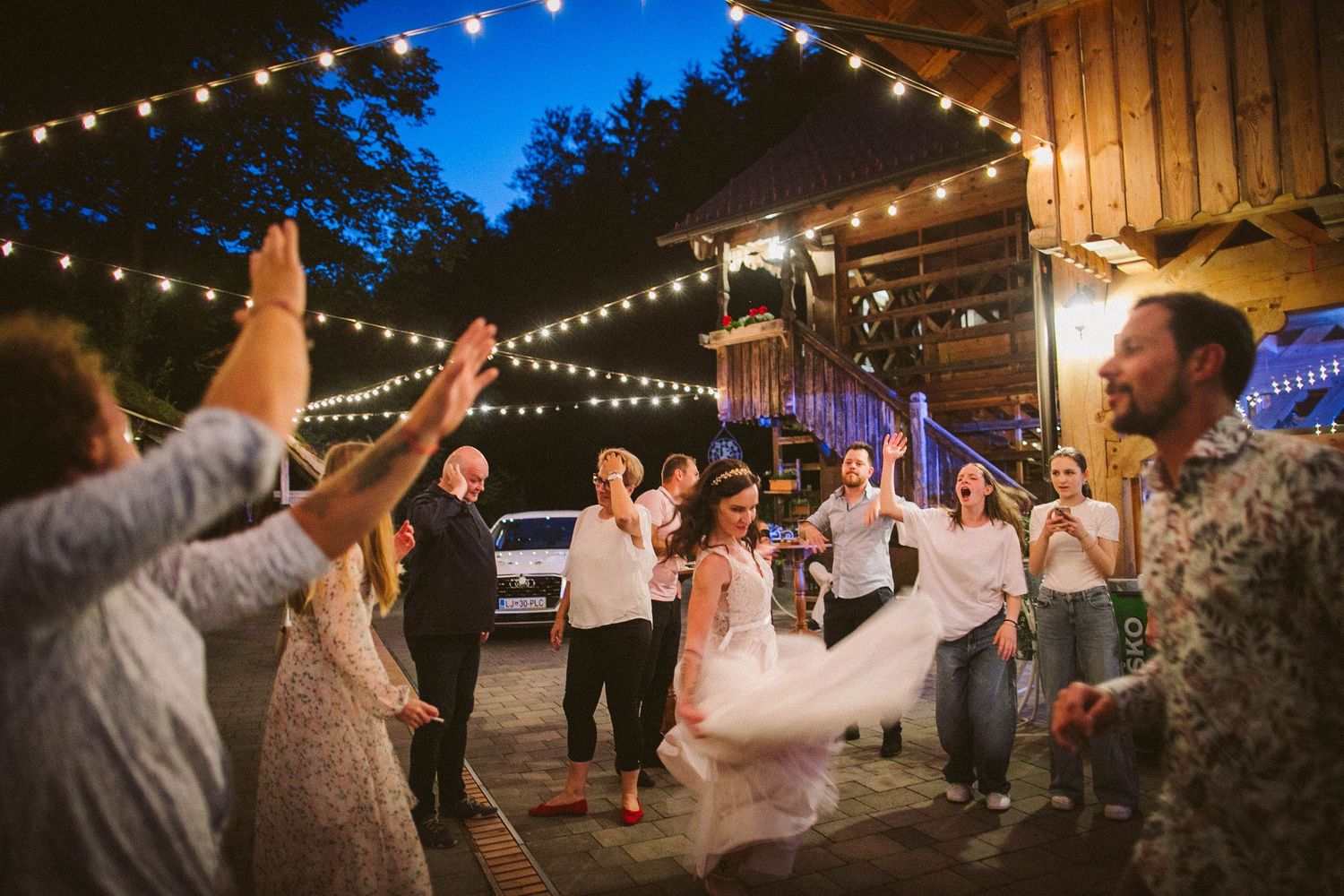 Wedding celebration under string lights at dusk with guests dancing outdoors.