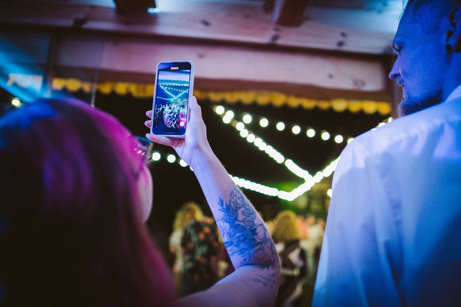 Guest takes a photo of string lights at wedding reception with illuminated phone screen.