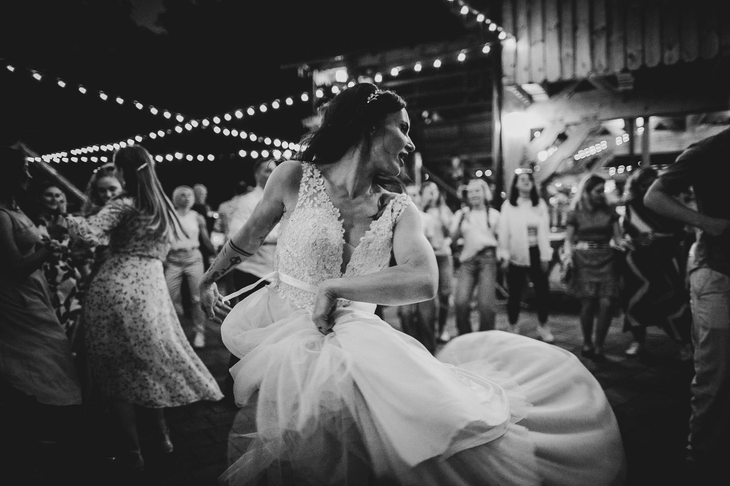 Dancing guests create a lively celebration under string lights at a rustic venue.