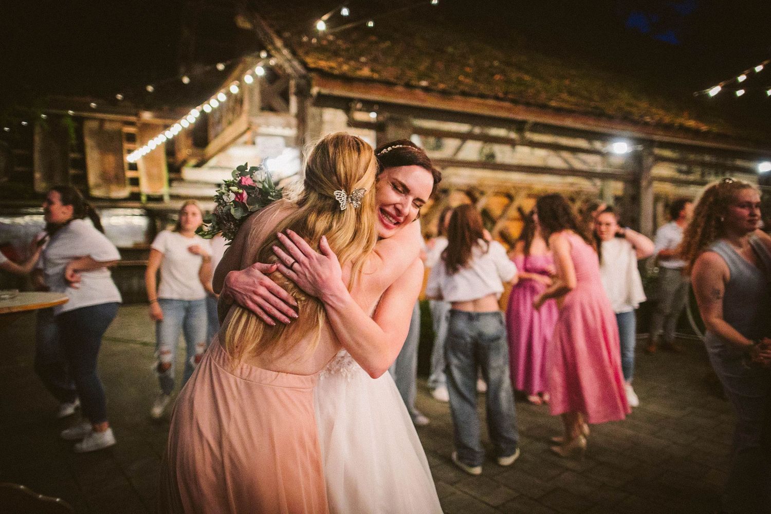Emotional moment during wedding reception as guests embrace under string lights.