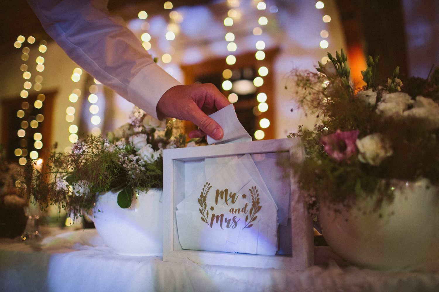 Wedding decor detail showing Mr & Mrs sign among floral arrangements and twinkling lights.