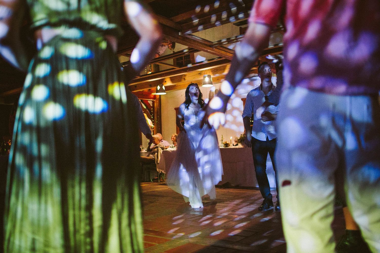 Dancers move across a rustic venue floor with dynamic lighting and shadows.