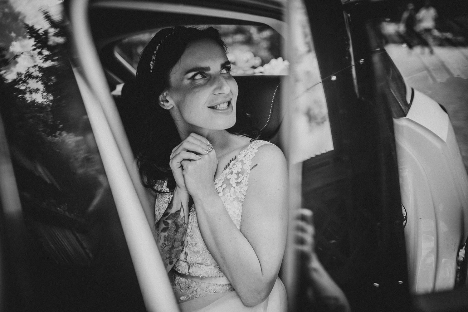 Candid black and white photo of a person sitting in a car wearing a wedding dress.