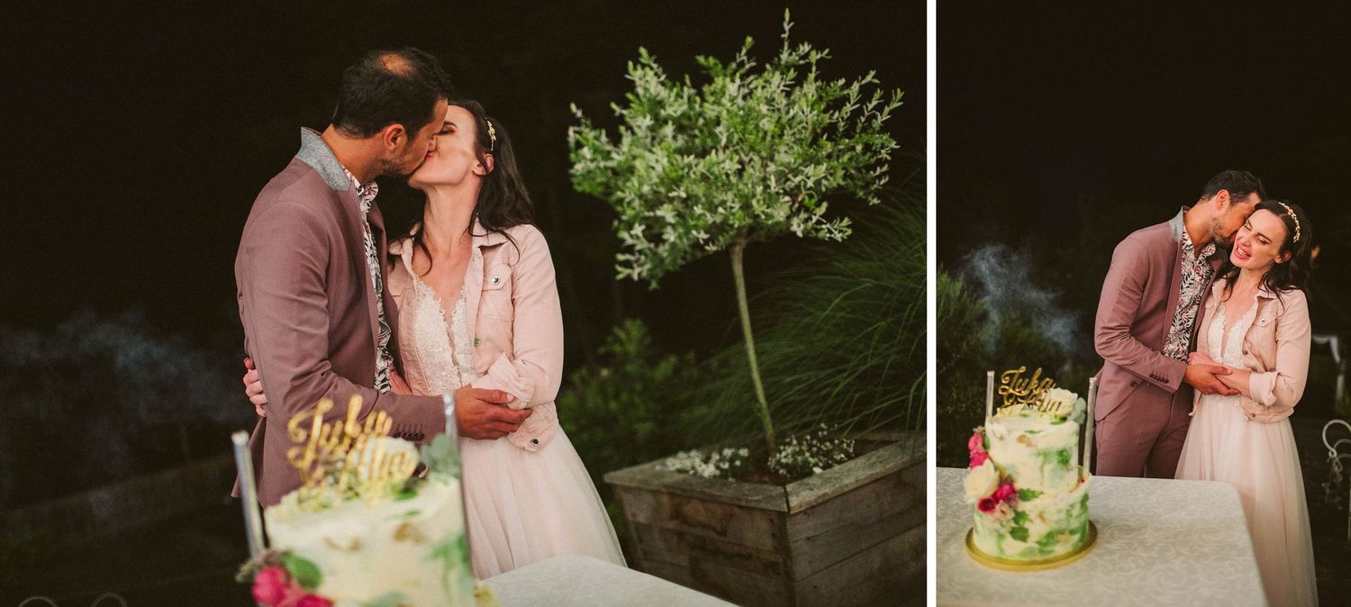 Couple sharing tender moment near wedding cake with green olive tree in outdoor evening setting.