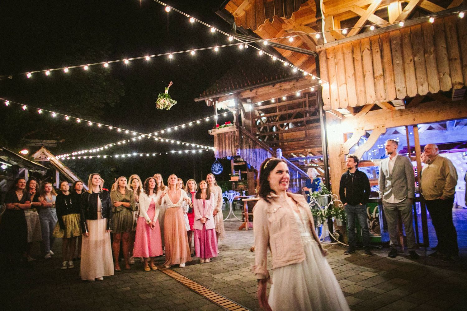 String lights illuminate a rustic barn wedding reception venue while guests gather on the dance floor for celebrations.
