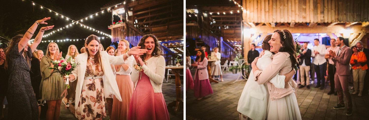 Wedding party members dance and celebrate under glowing string lights at a rustic barn reception venue.
