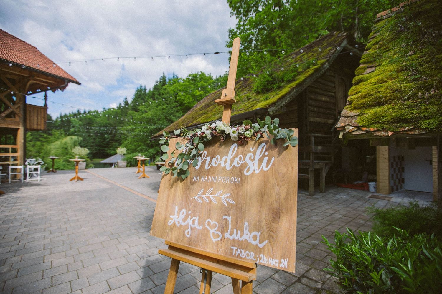 Wooden welcome sign with floral decorations at an outdoor rustic wedding venue.