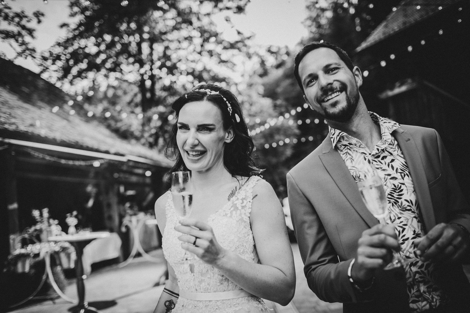 Black and white photo of wedding guests celebrating with drinks under string lights.