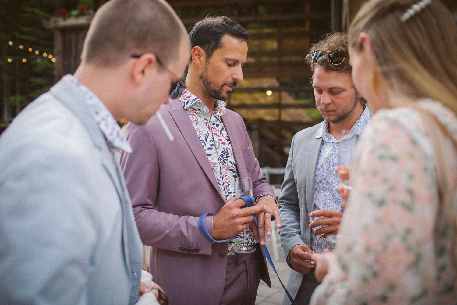 Small group socializing at outdoor reception with guest in floral shirt and mauve blazer.