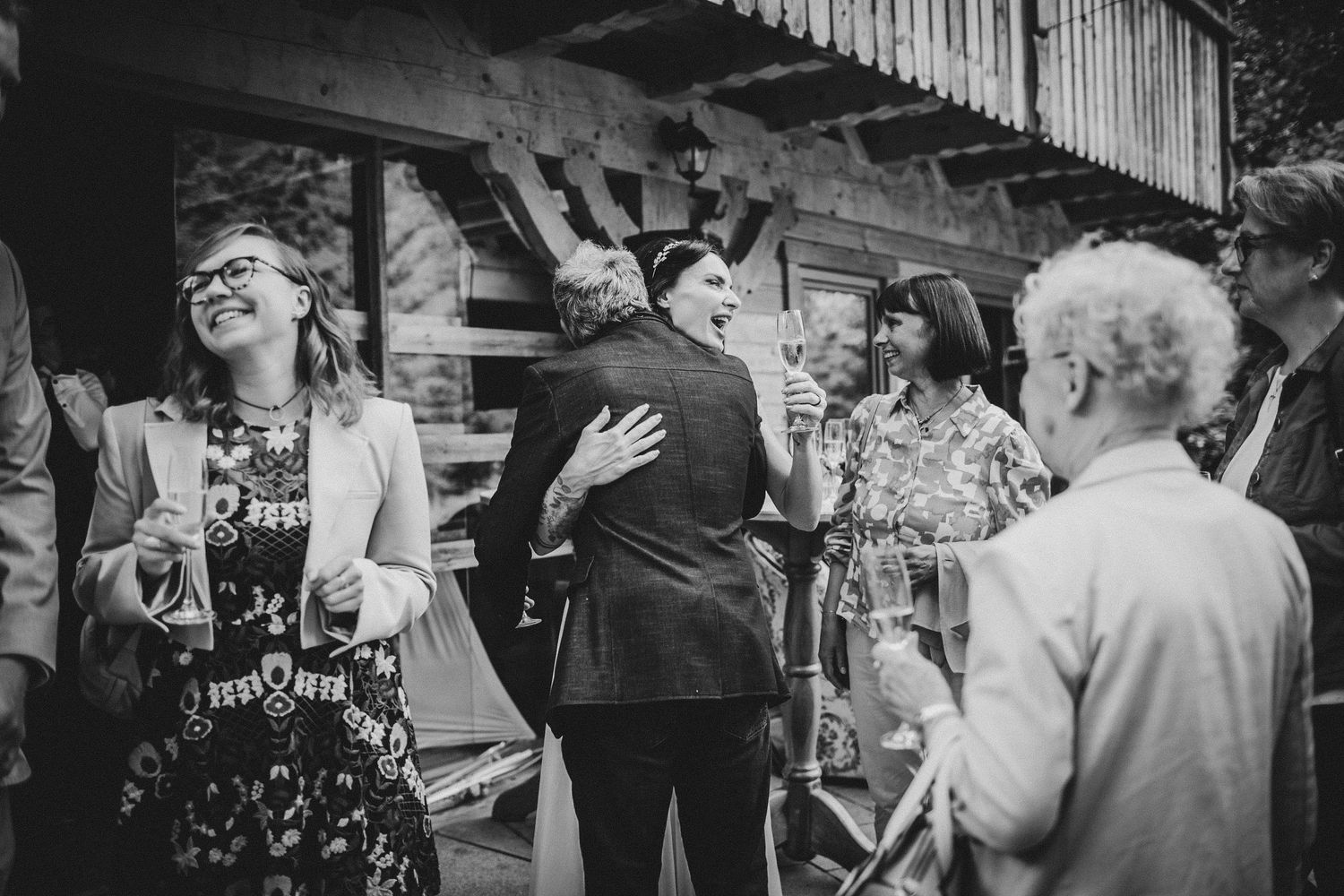 Black and white candid photo of guests mingling and laughing at outdoor garden party.