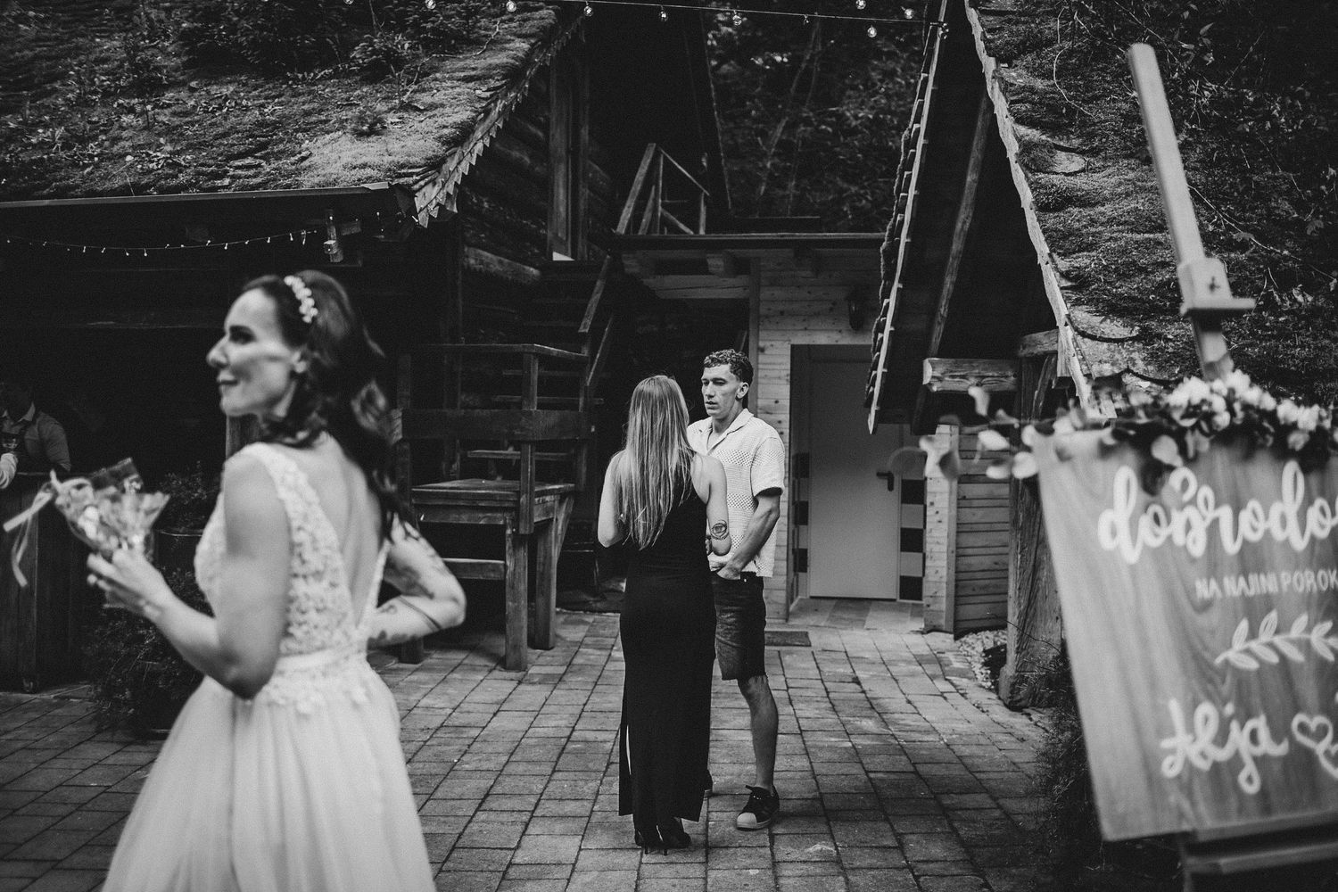 Guests gather on a patio near a rustic wooden building during a celebration.