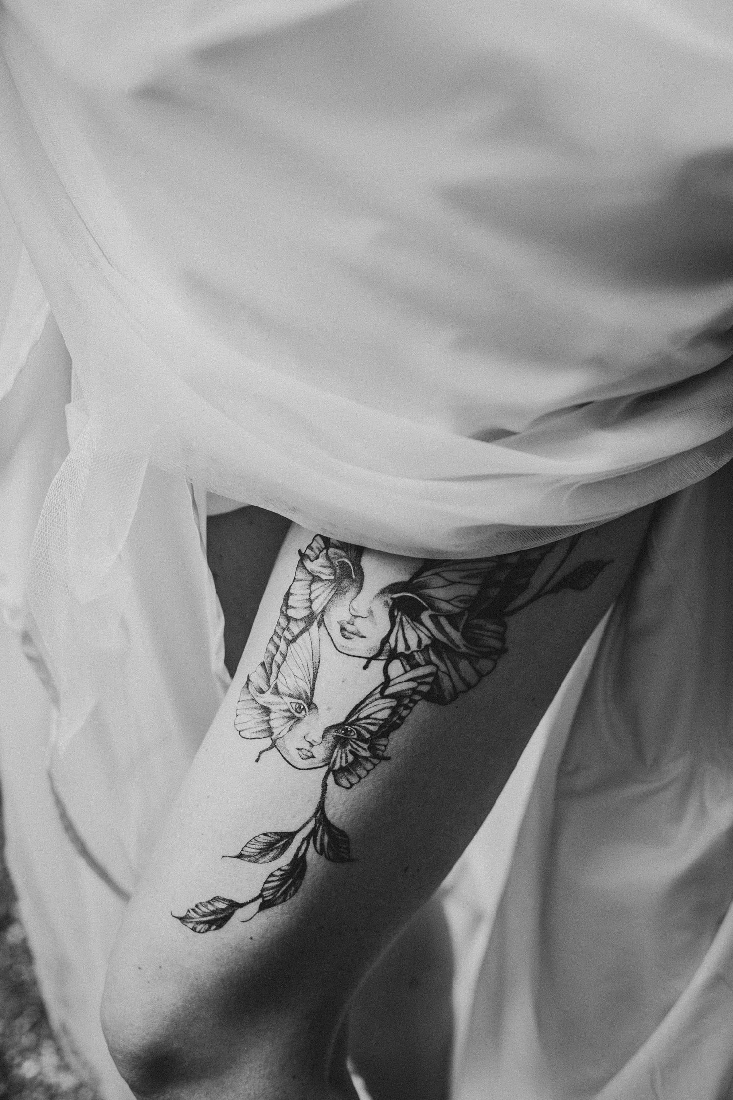 Close-up black and white photo of artistic tattoo under wedding dress fabric.