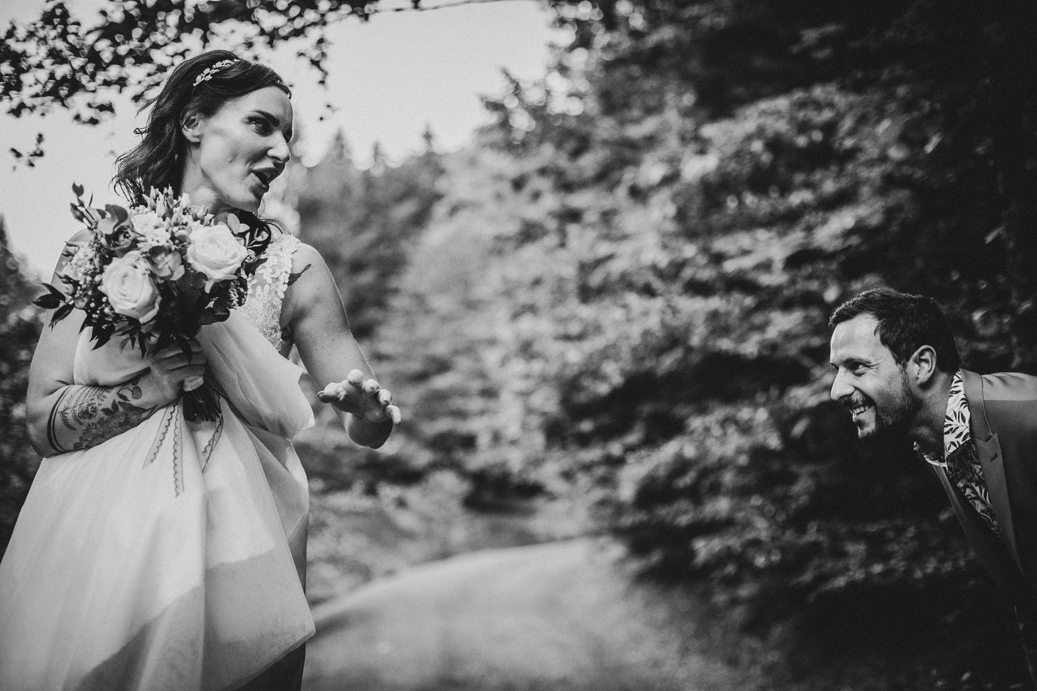 Black and white candid photo of joyful interaction between wedding couple on forest path.
