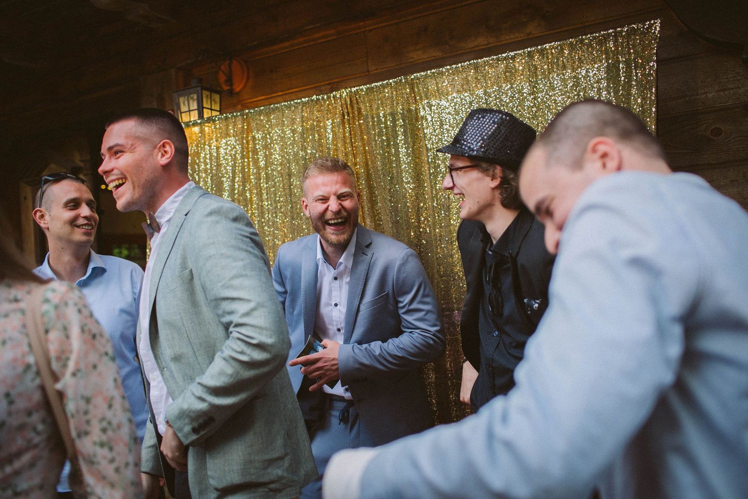 Casual wedding gathering with guests laughing against a gold sequin backdrop.
