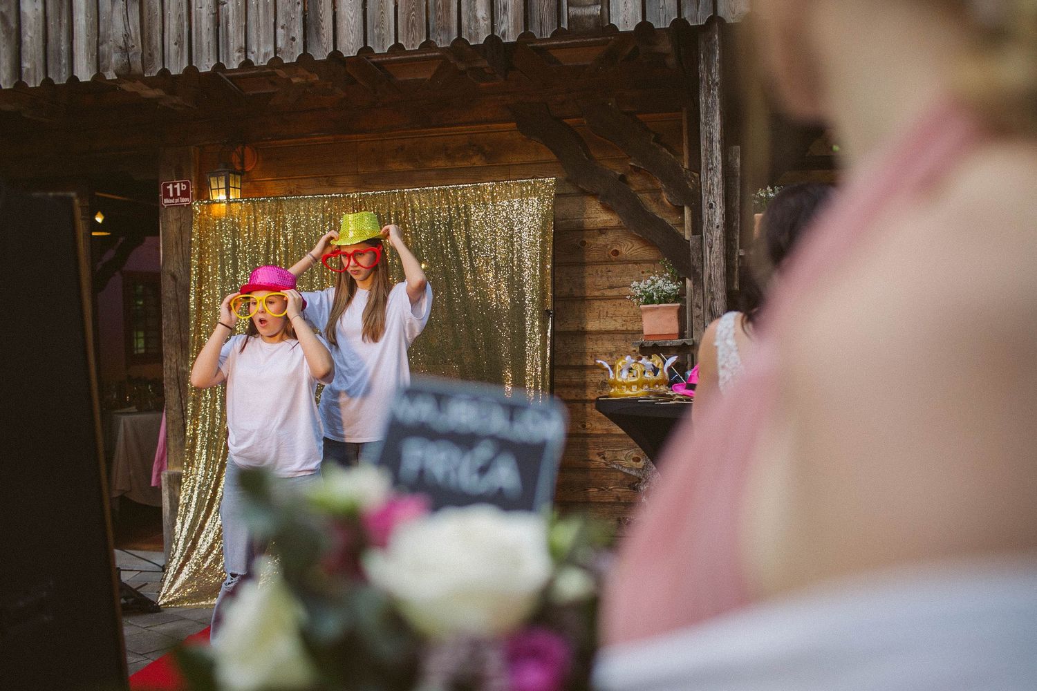 Wedding reception features guests celebrating in front of a rustic wooden backdrop with string lights.
