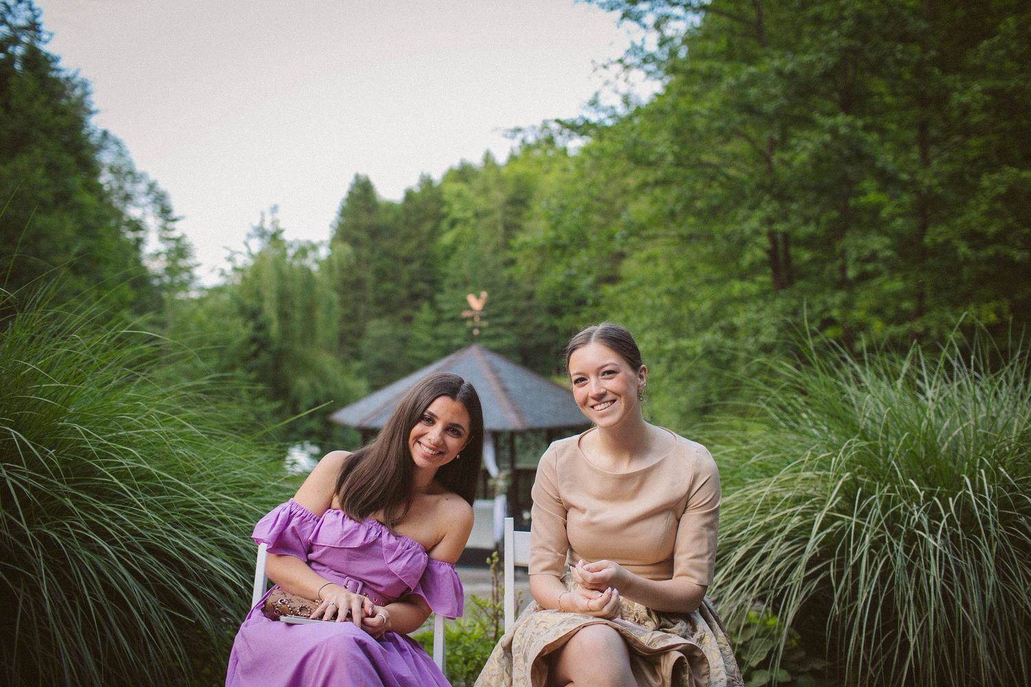 Two people sitting outdoors surrounded by tall ornamental grasses in a natural setting.