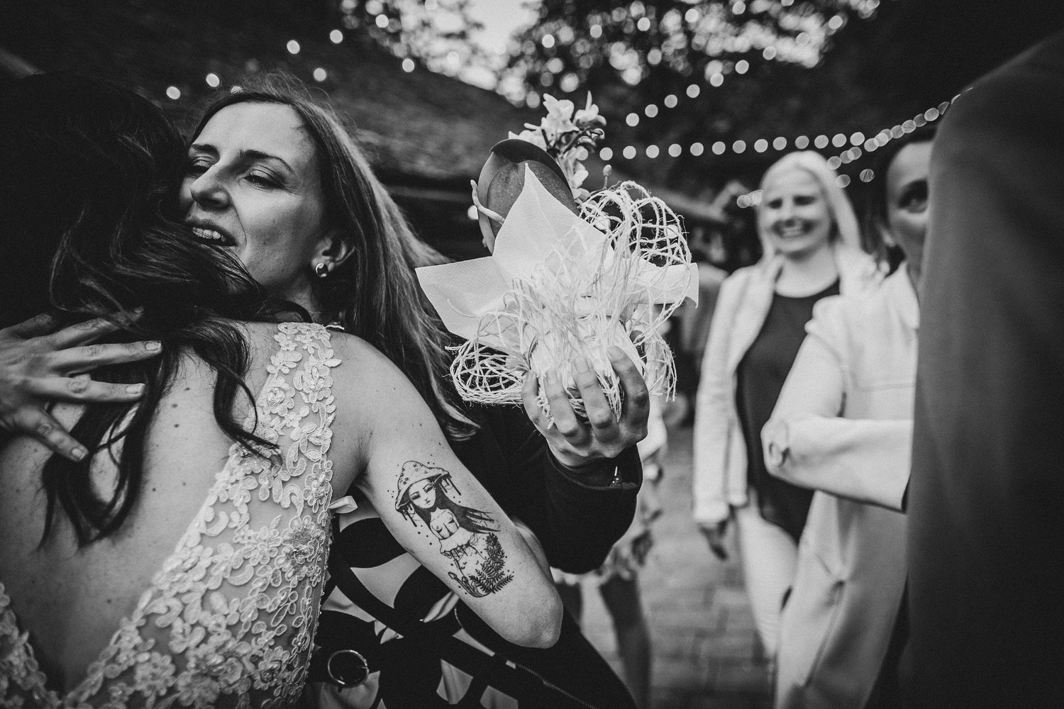 A dramatic black and white shot of people dancing at an outdoor party with string lights visible.