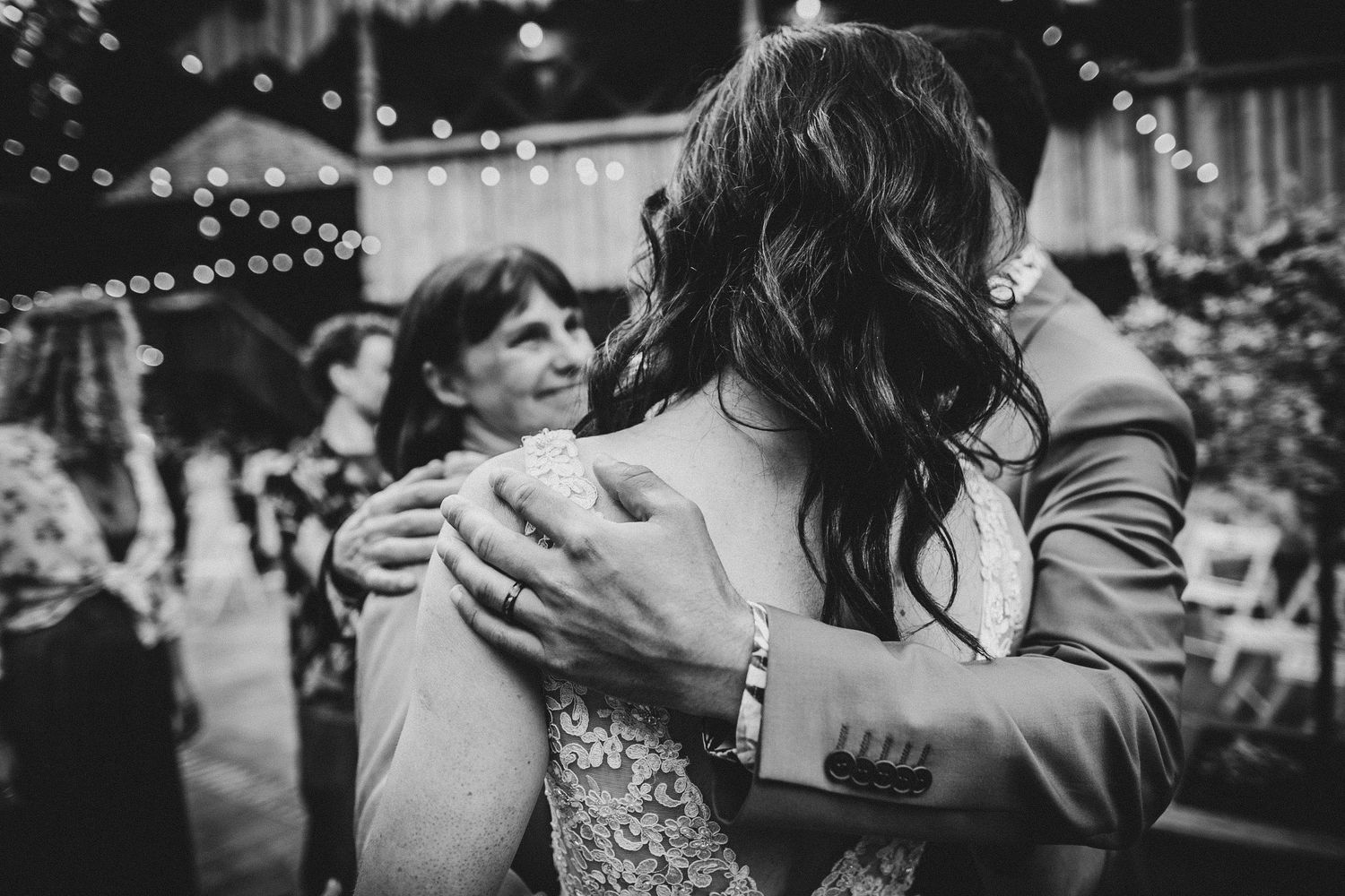 Black and white capture of an emotional embrace during evening celebration under string lights.