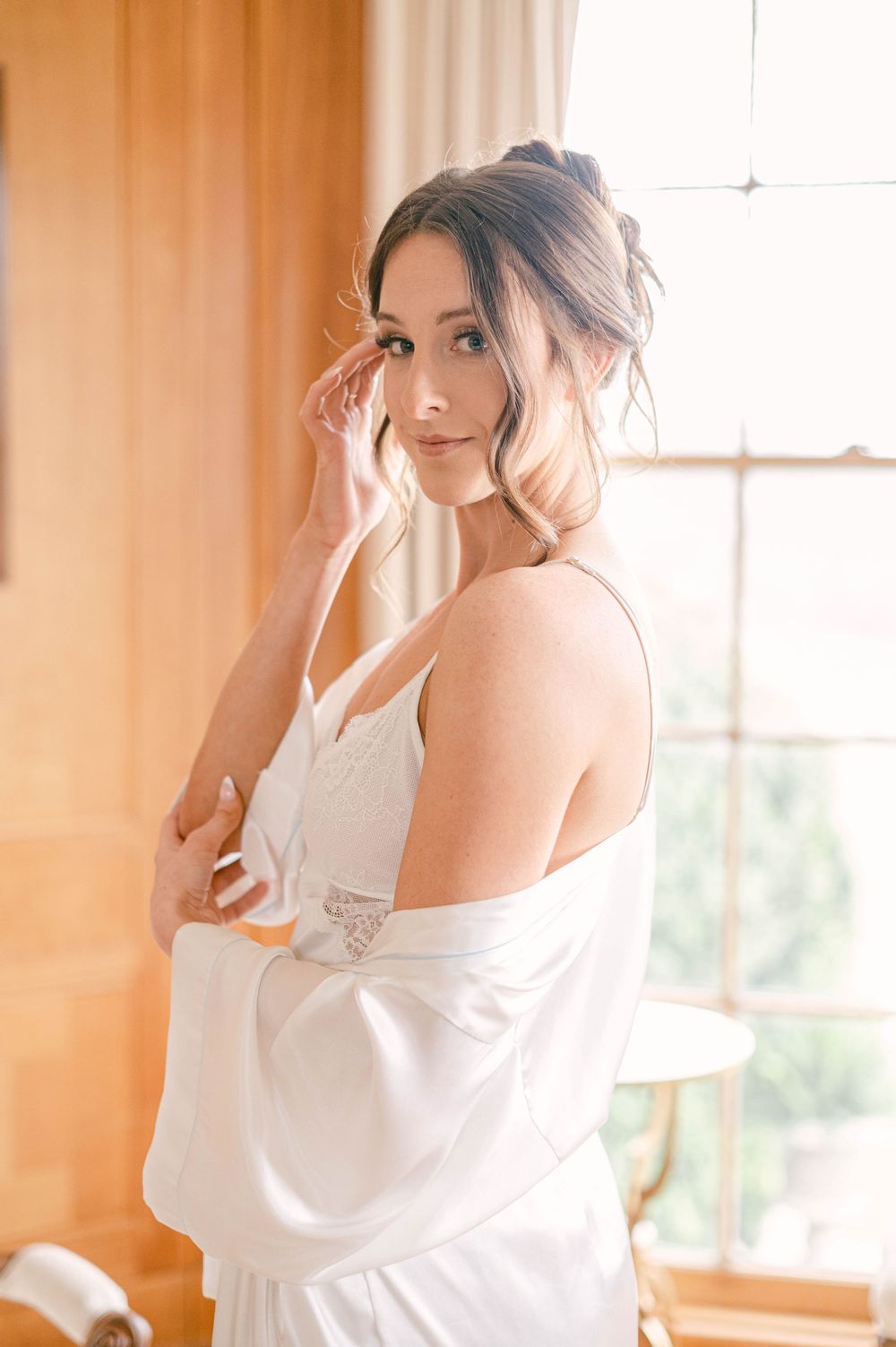 A soft morning light illuminates a delicate white silk robe and elegant bridal attire.