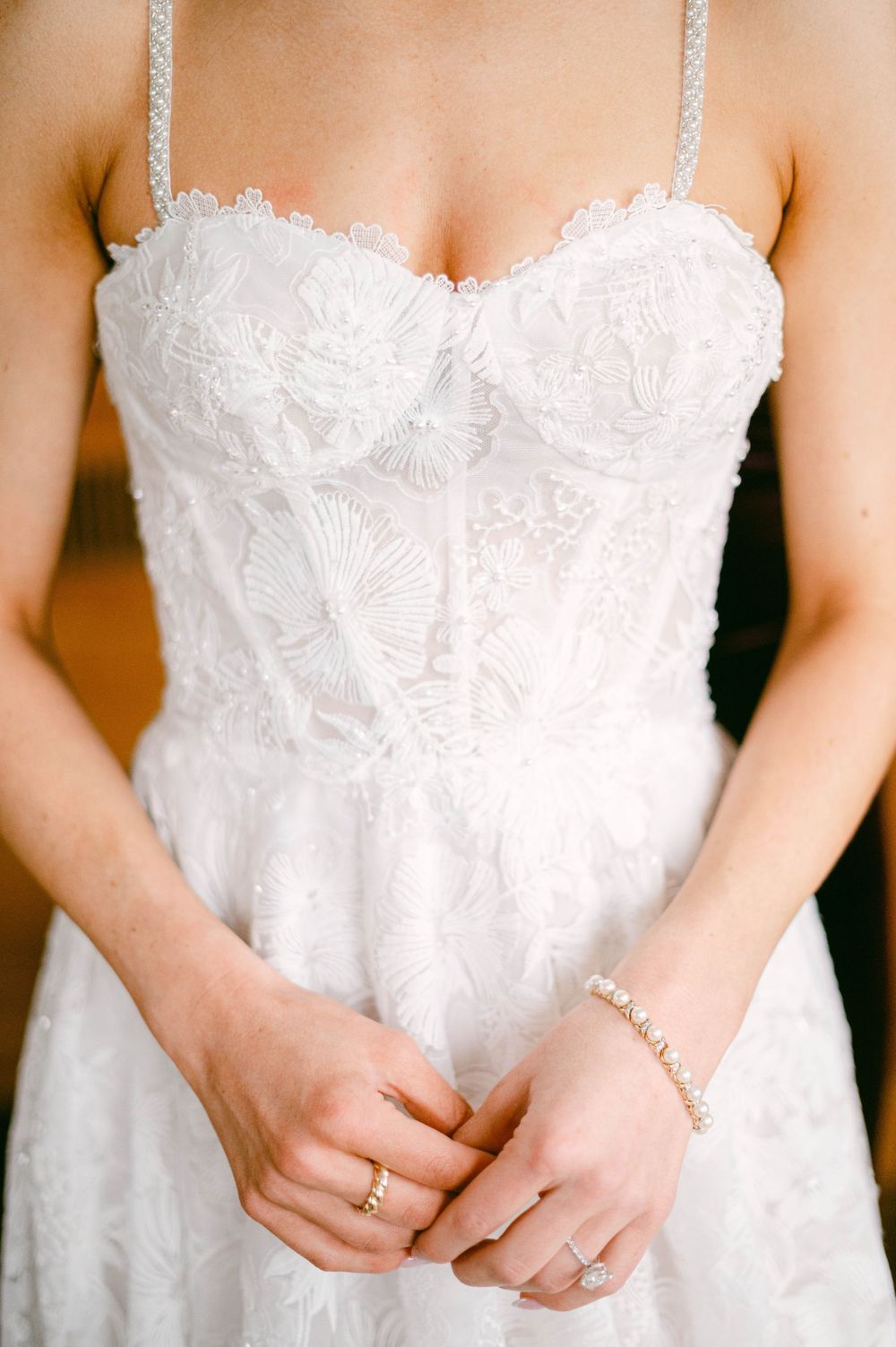 A bride in a classic lace wedding gown being helped with final preparations.