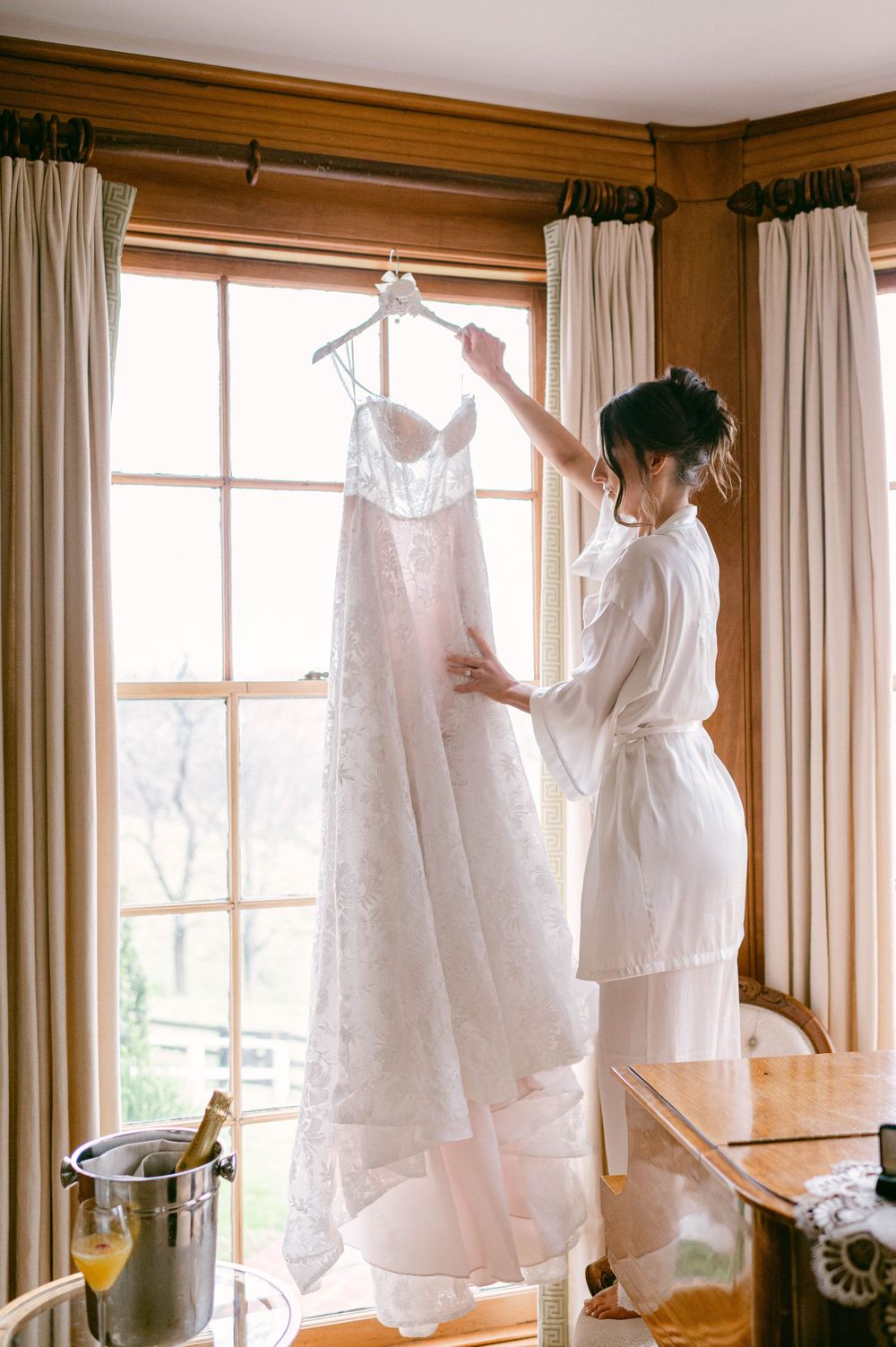 White vintage dresses displayed on hangers against windows in a sunny room with wooden walls.
