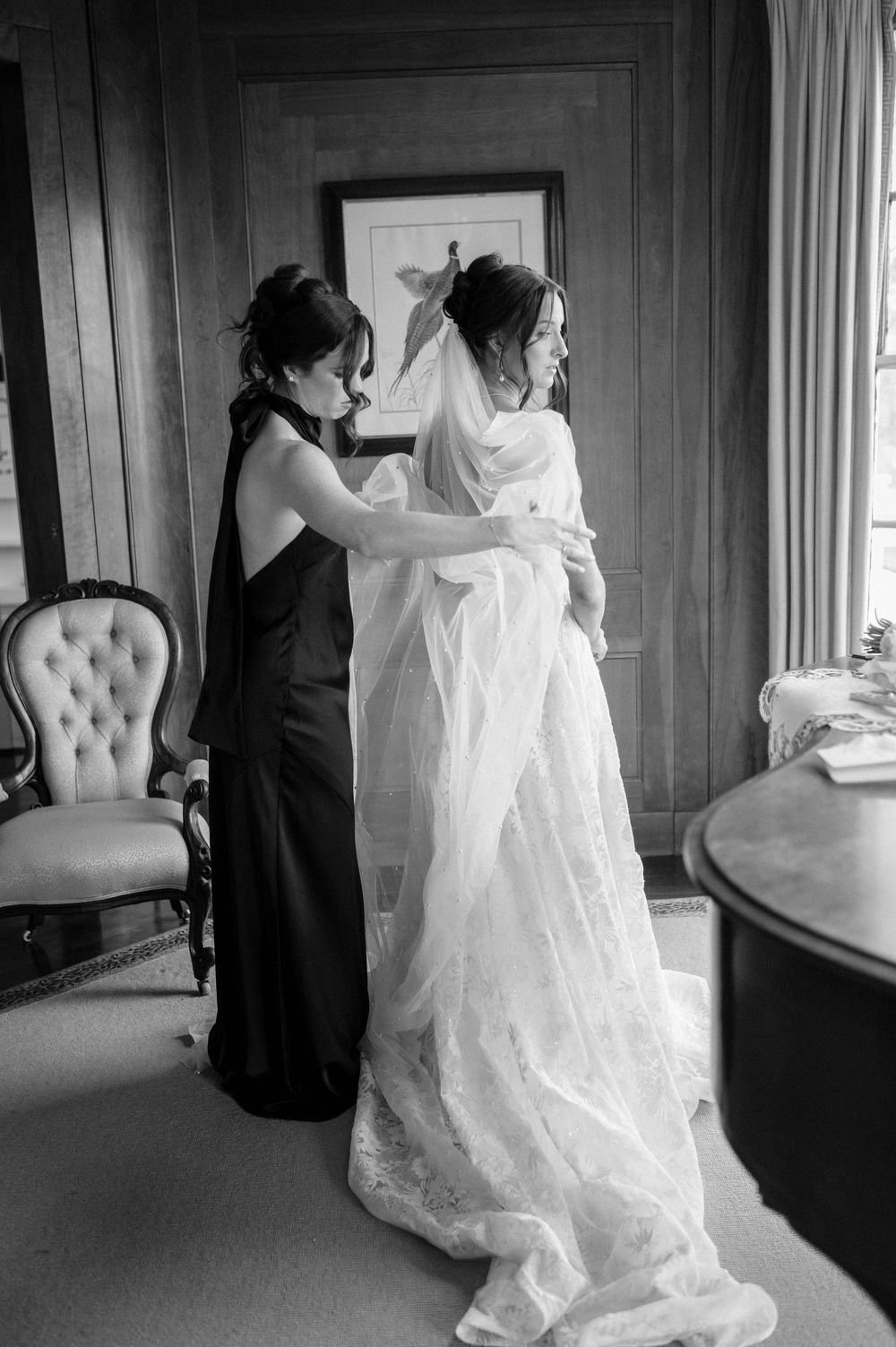 Black and white series showing wedding dress preparation in an elegant room.