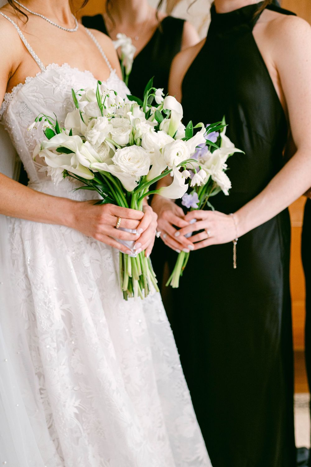 Close-up of wedding party holding white bouquets, contrasting black dresses with white bridal gown.