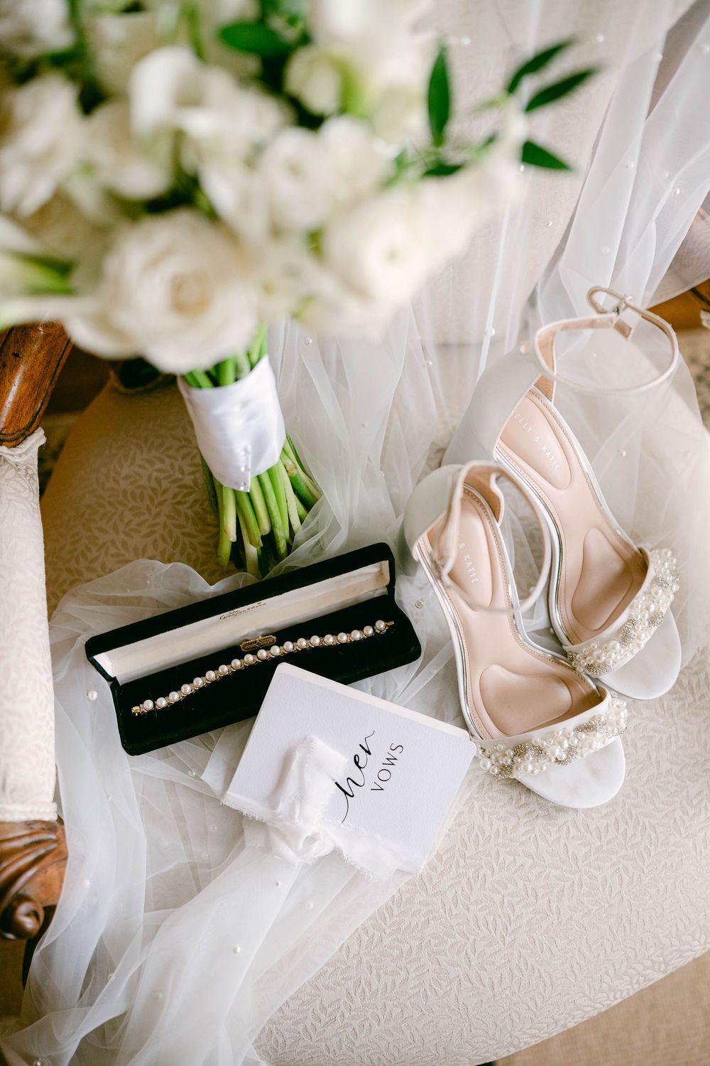 Wedding accessories including white roses, pearl jewelry, and delicate blush bridal shoes.