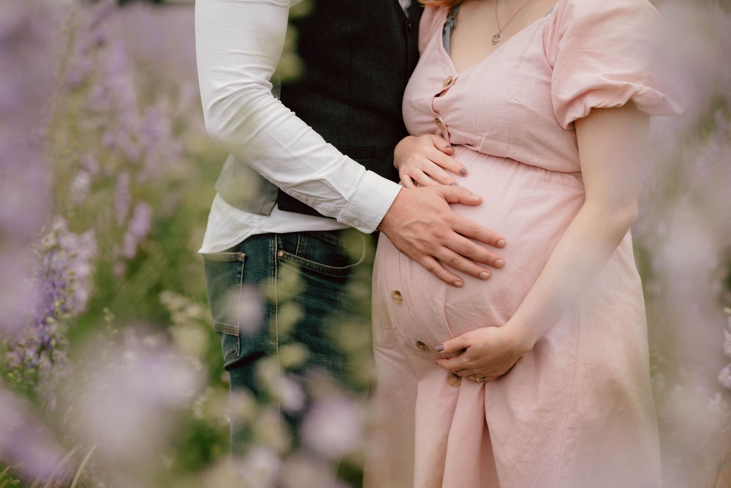 A loving family smiles together while sitting in a field of beautiful purple wildflowers during a summer photoshoot.