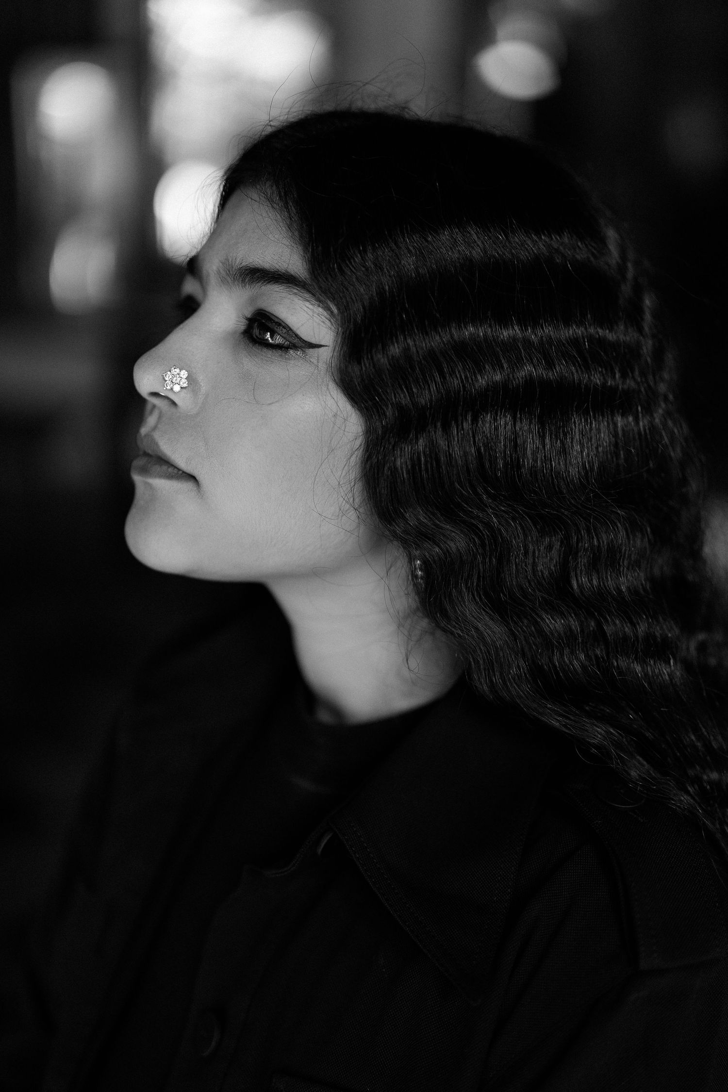 Dramatic black and white portrait in profile view showing vintage-inspired finger waves hairstyle and rhinestone detail.