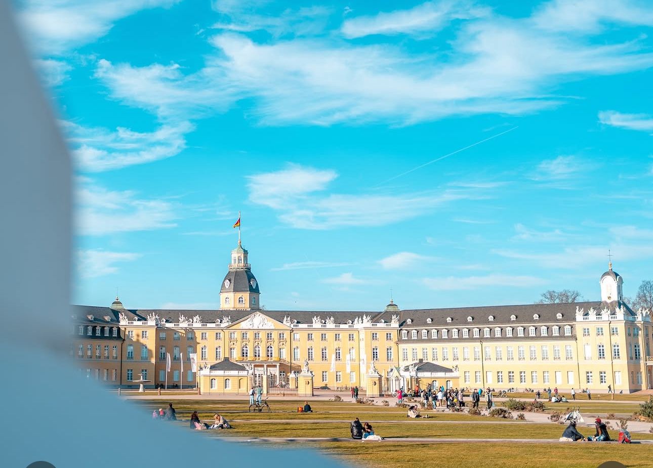 Hochzeitspaar beim Fotoshooting vor dem Schloss Karlsruhe mit barocker Fassade und Schlossgarten im Hintergrund.