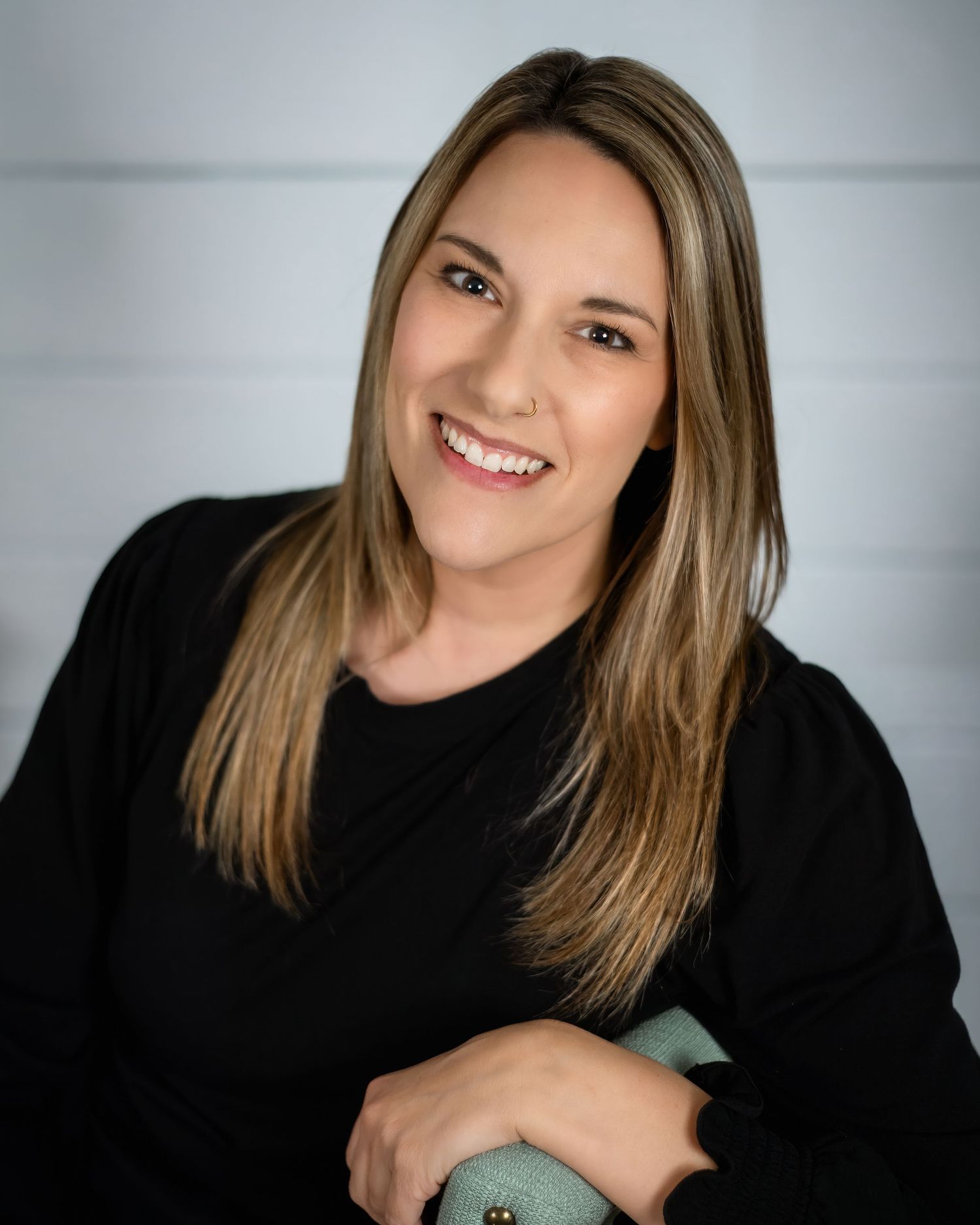Professional headshot on gray backdrop shows a warm smile wearing a dark navy crewneck sweater.