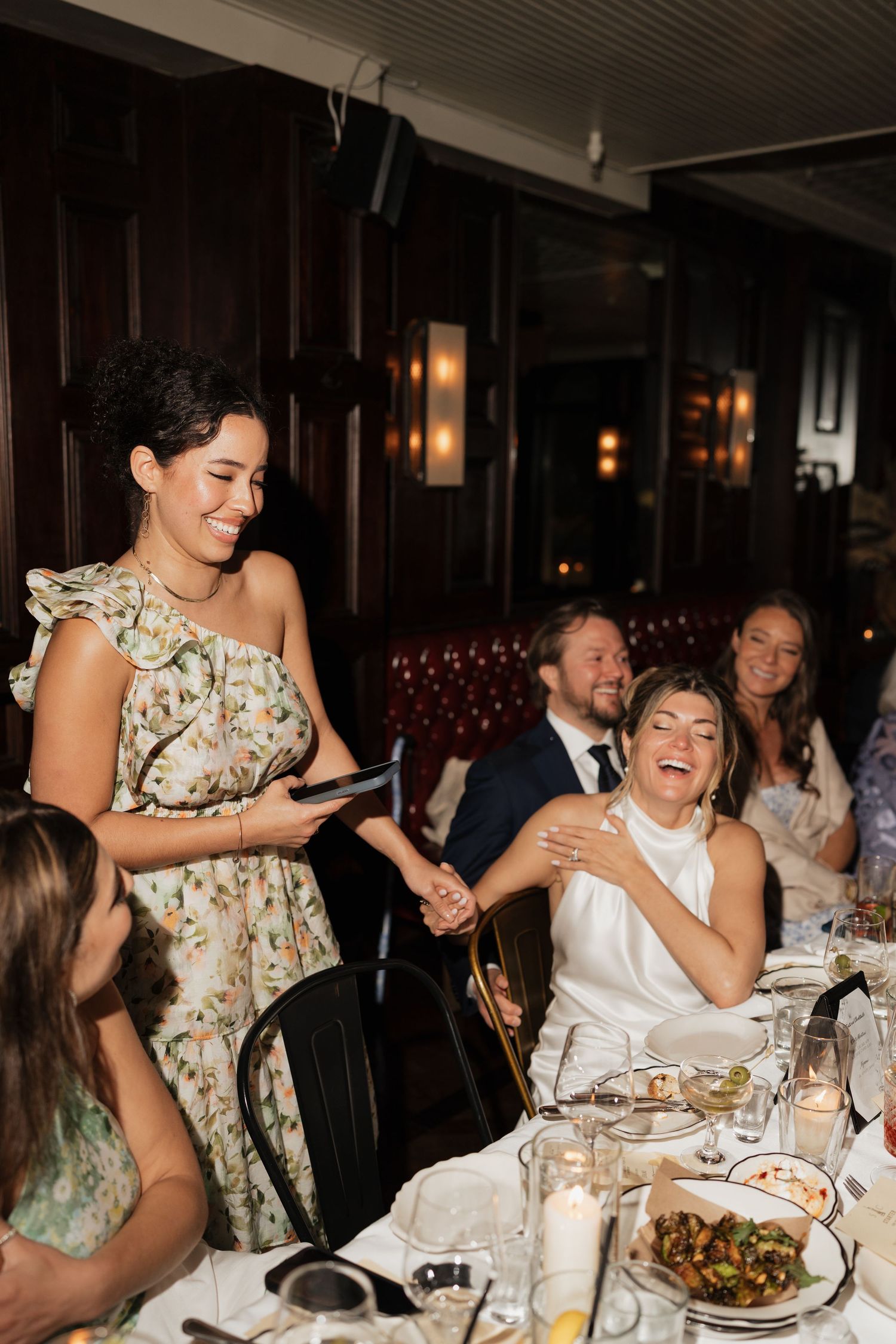 Guests sharing laughter and joy during a dinner party at an elegant restaurant with warm lighting and leather booth seating.