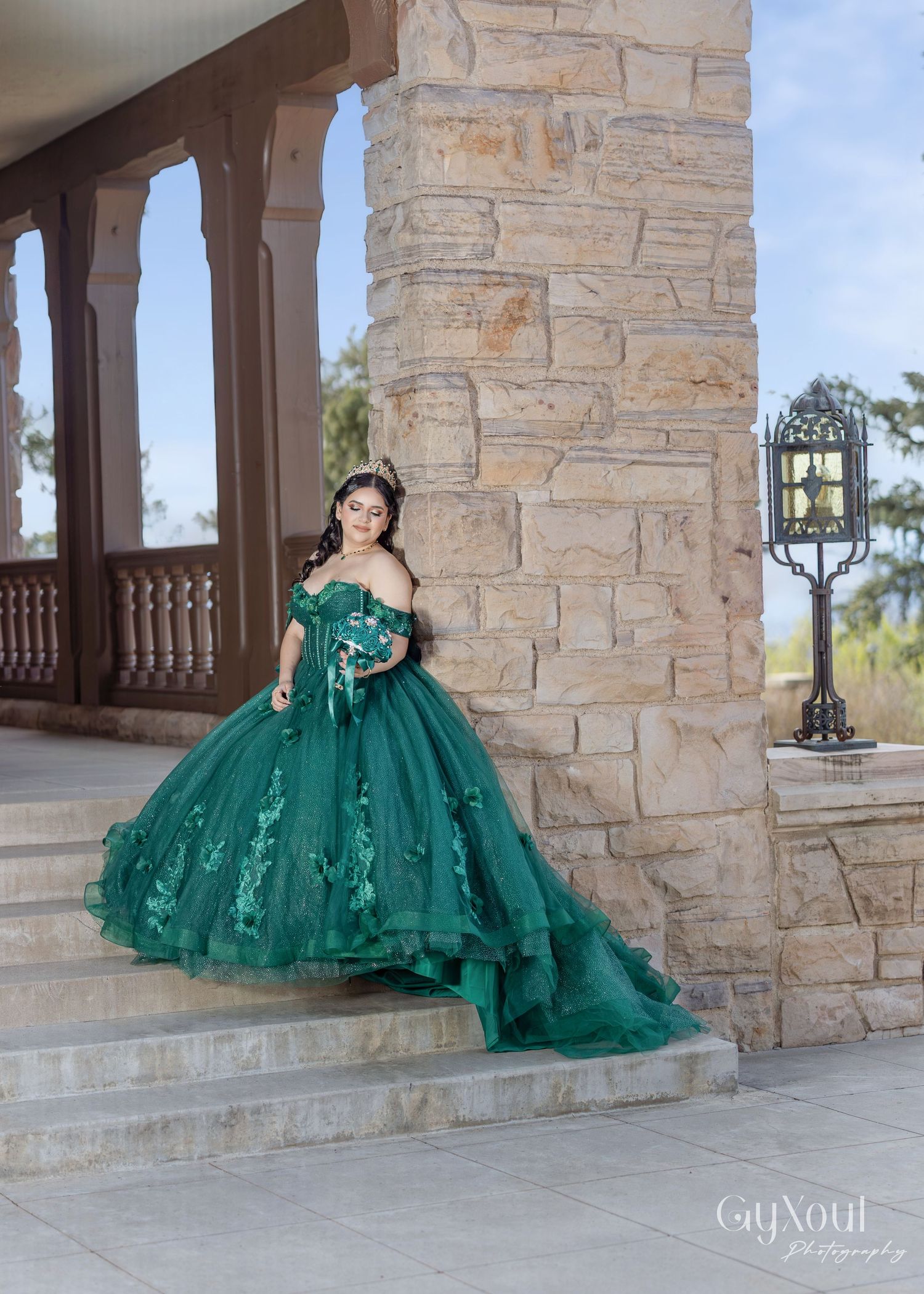 An emerald green ball gown with intricate floral details sits elegantly on stone steps by an outdoor lantern.