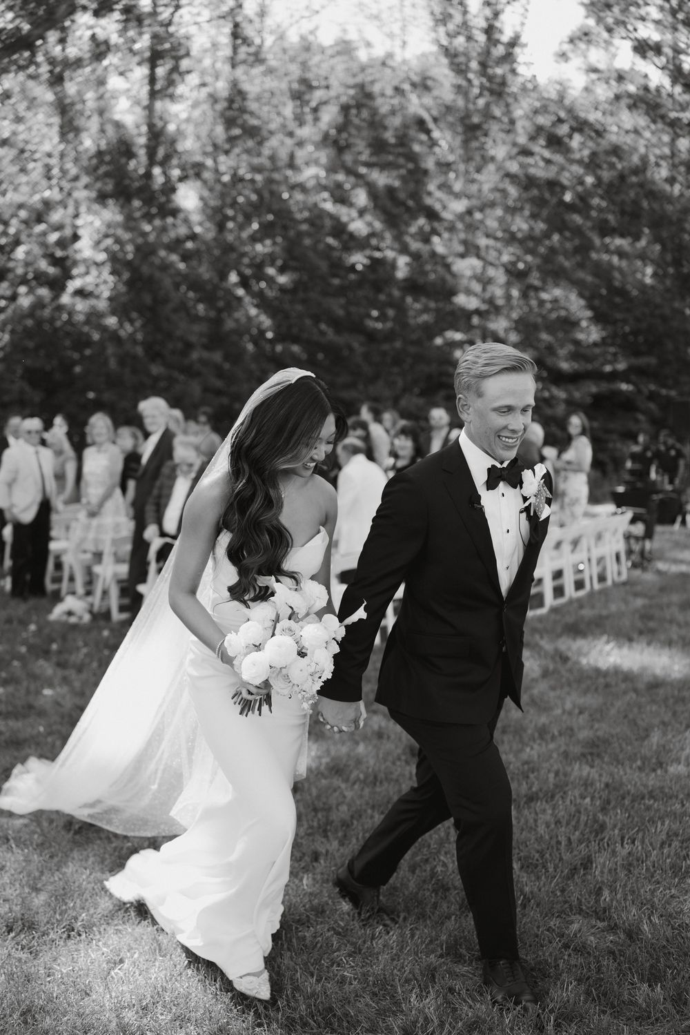 Black and white photo of a couple running playfully through a grassy field.