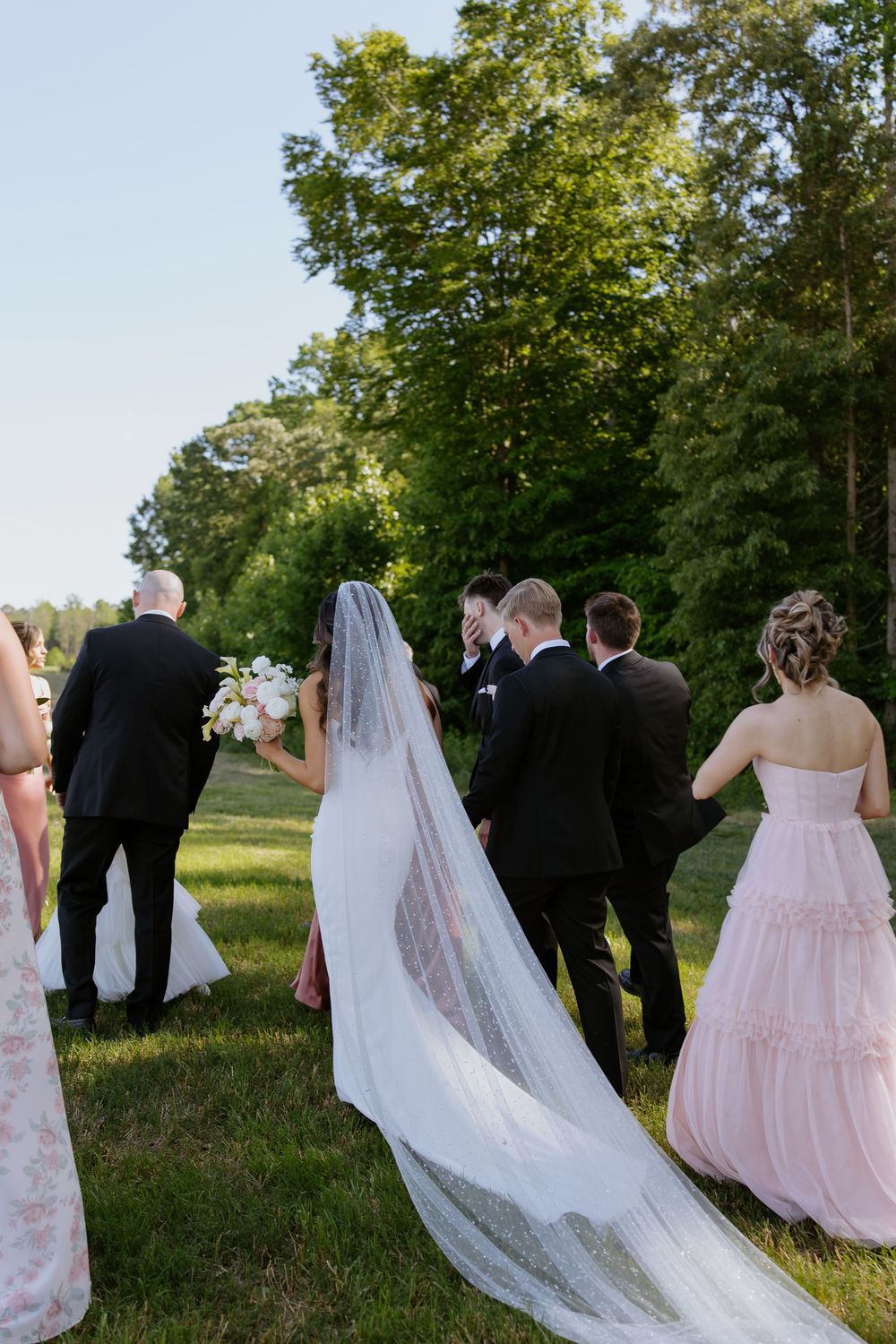 Wedding party walking together on a grassy hillside during golden hour.