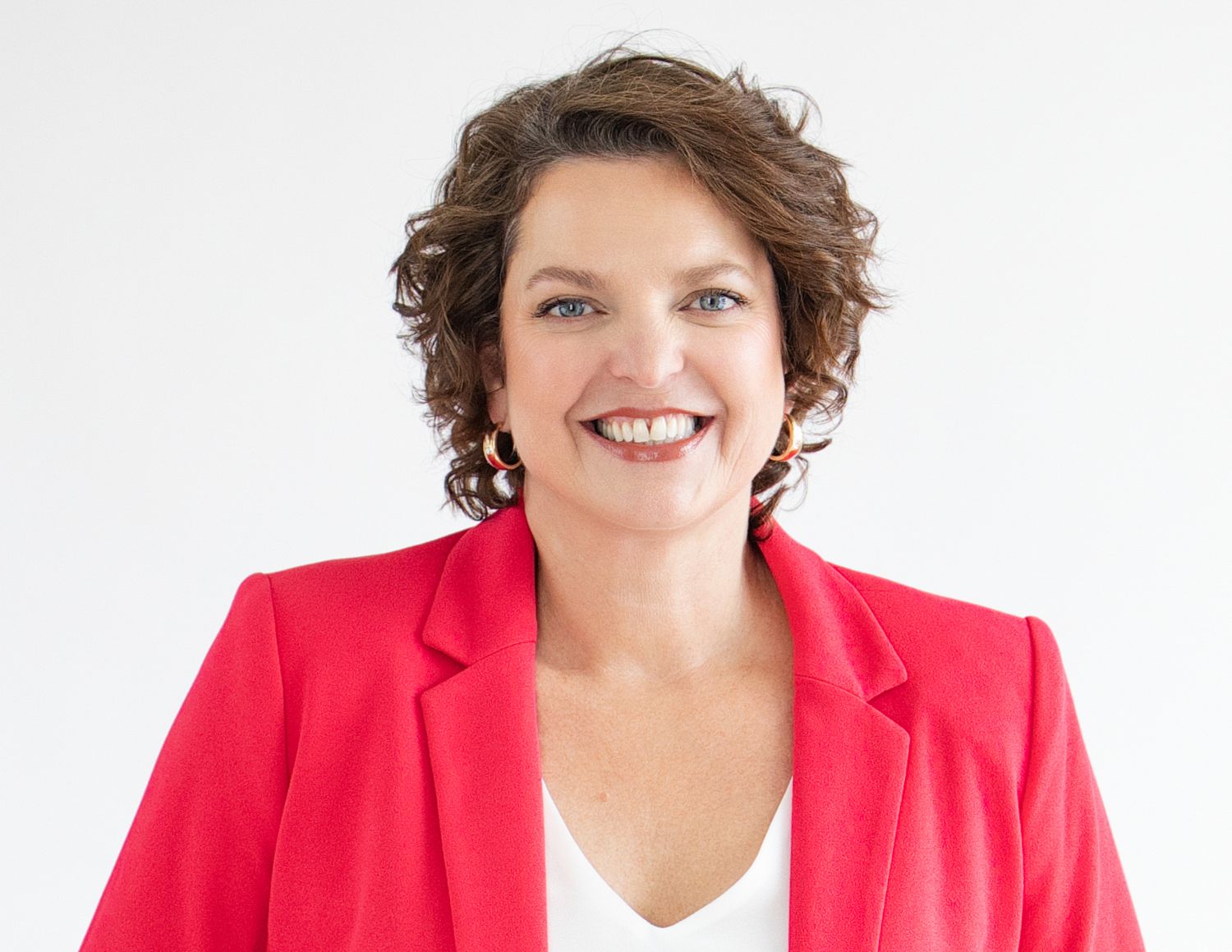 Professional headshot of Jennifer McCallum business coach for coaches wearing a pink blazer with dark short curly hair.