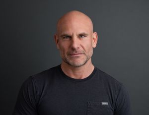 Dynamic headshot of bald professional man with a dark grey backdrop by captured by Thea in London Ontario