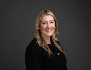 corporate team headshots of woman with blonde hair and dark sweater on dark paper backdrop