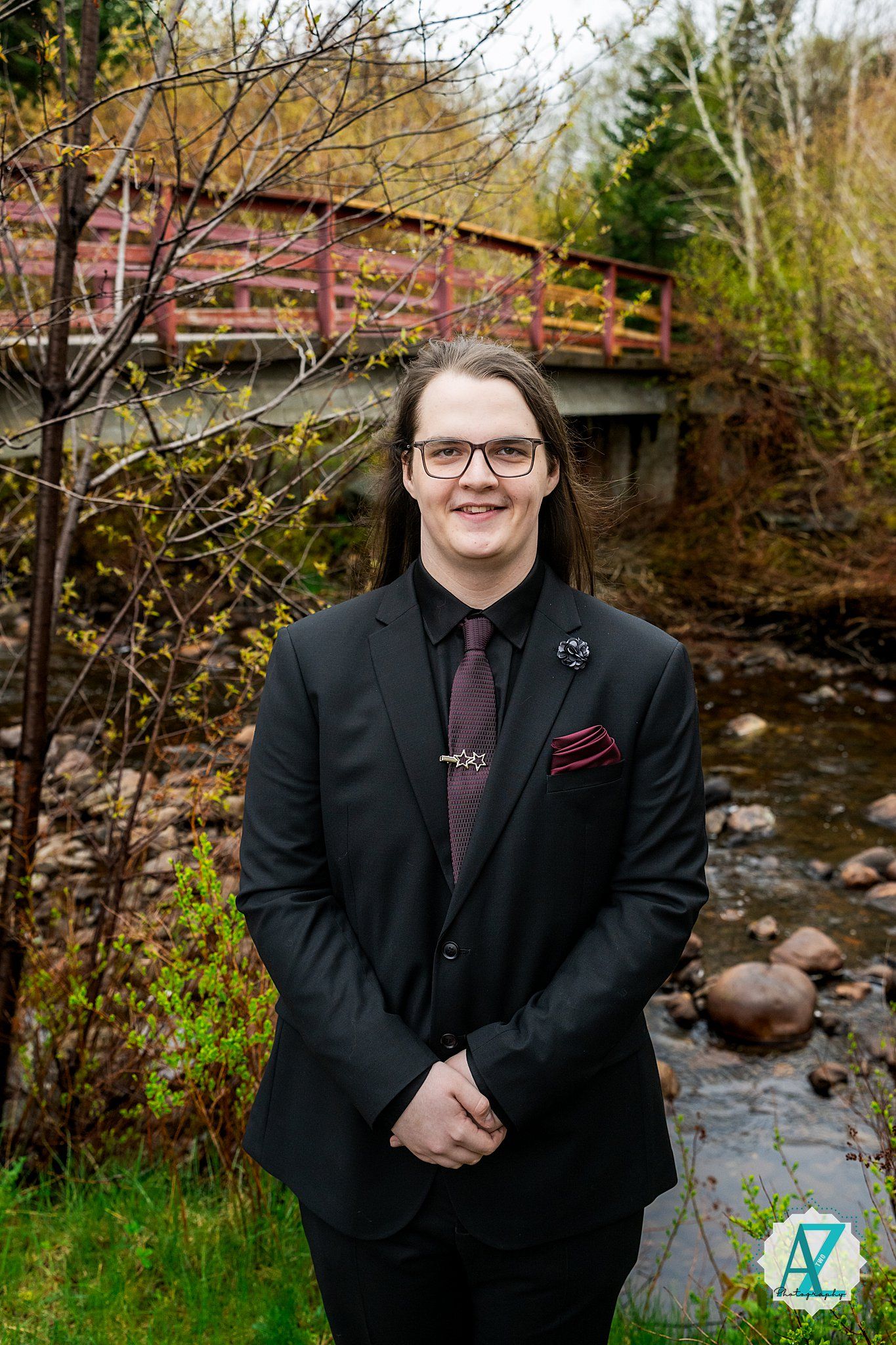 Outdoor portrait near a rustic wooden bridge over a rocky stream in autumn with evergreen trees in the background.