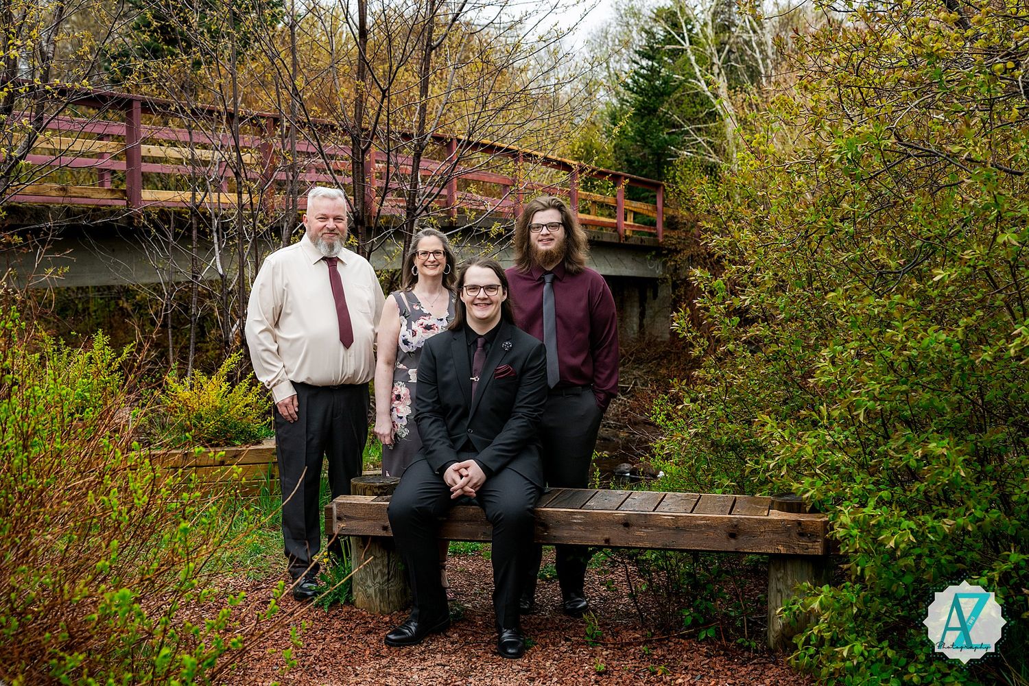 A group stands together on wooden stairs near a rustic wooden bridge surrounded by autumn foliage in a park setting.