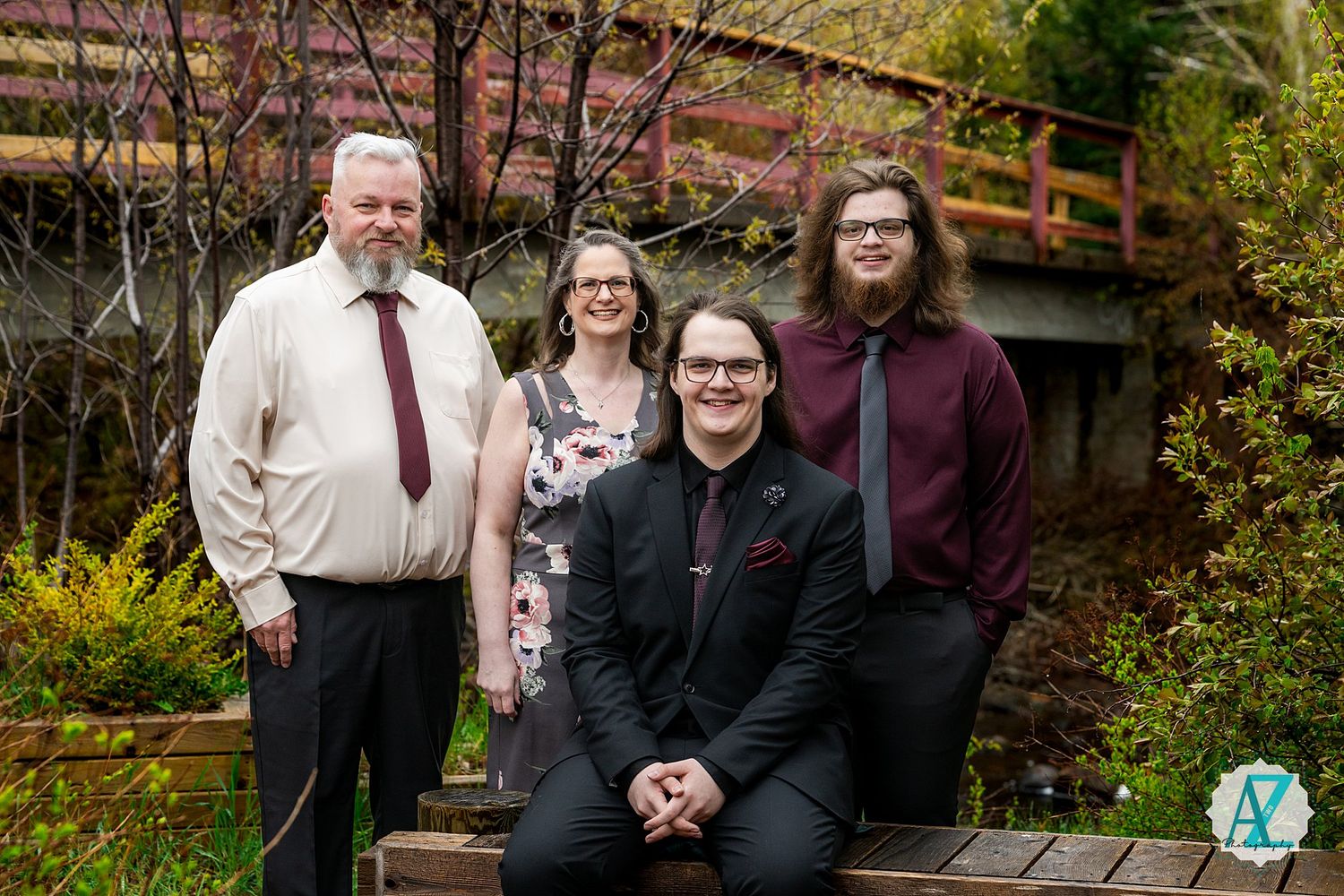 A group stands together on wooden steps in a garden with a footbridge and autumn foliage in the background.