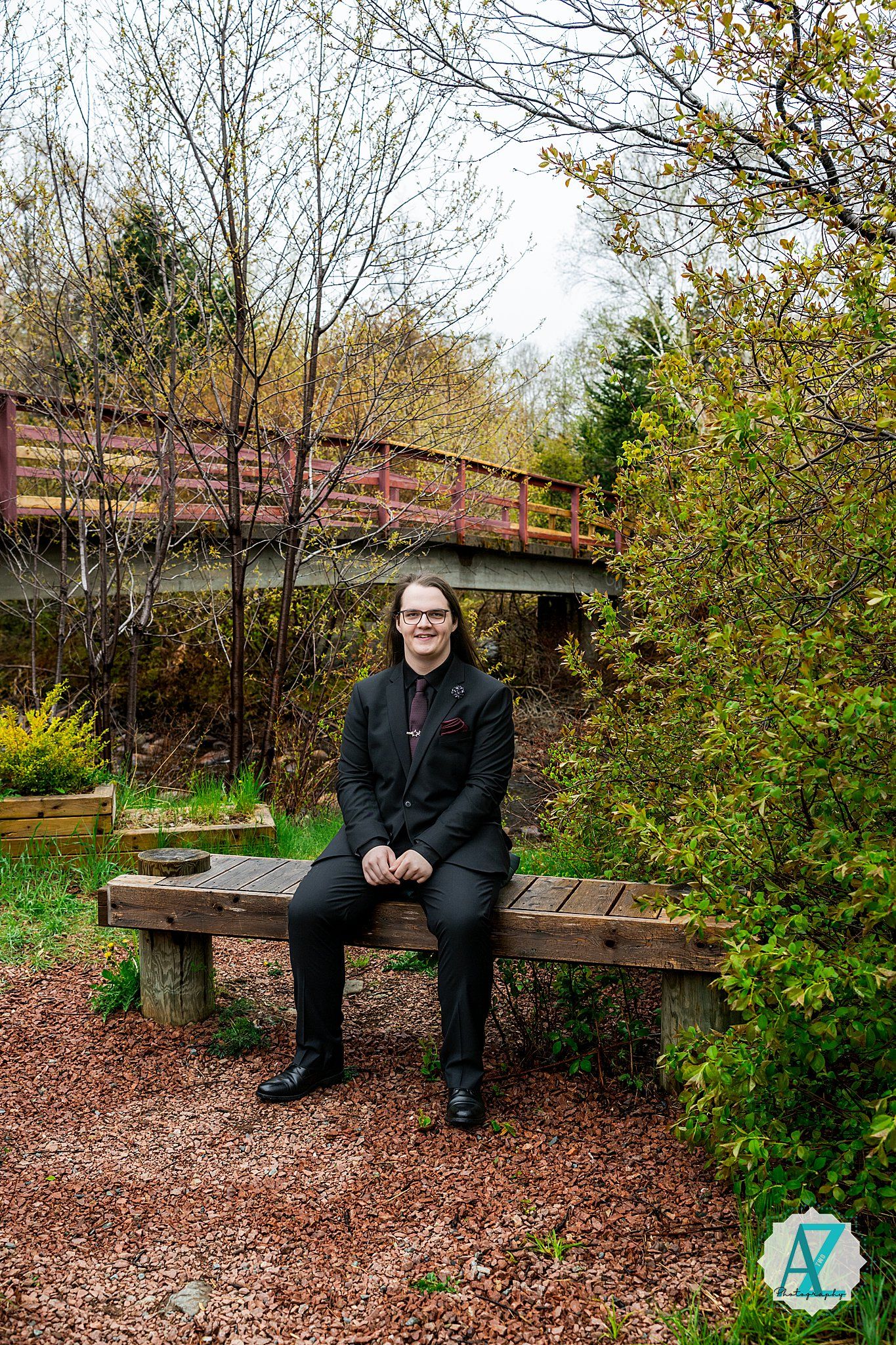 Person sitting on wooden bench along garden path with red wooden bridge in background during autumn season.
