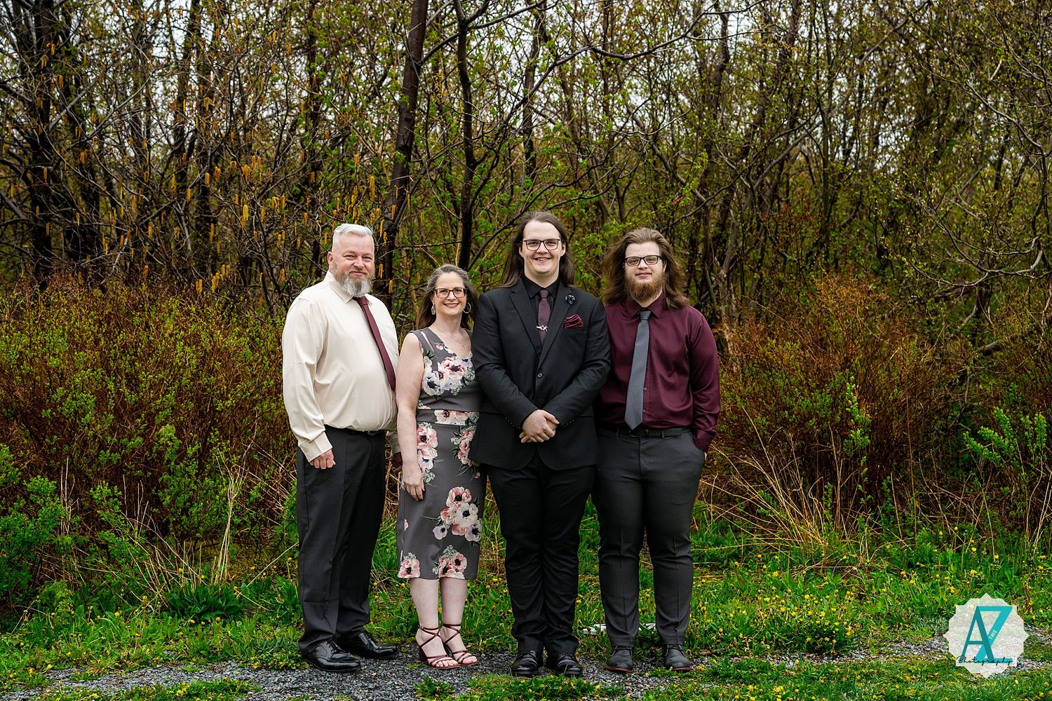 A group of four people stand together for a portrait outdoors against a backdrop of autumn trees and greenery.