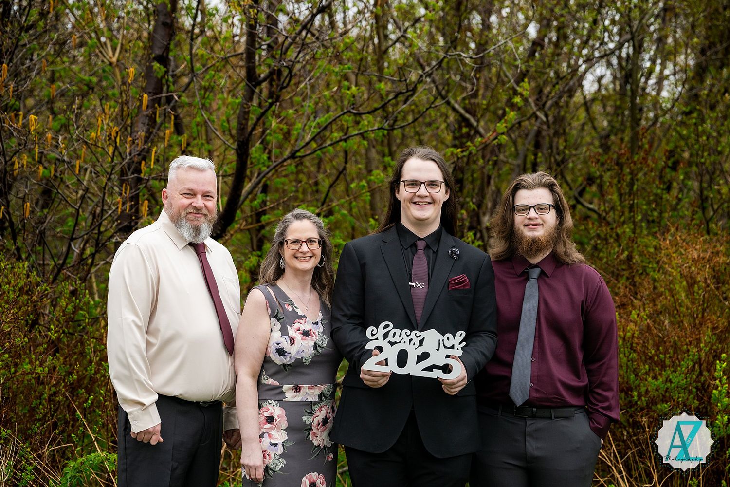 A group of four people pose outdoors with a graduation 2023 sign among autumn foliage.