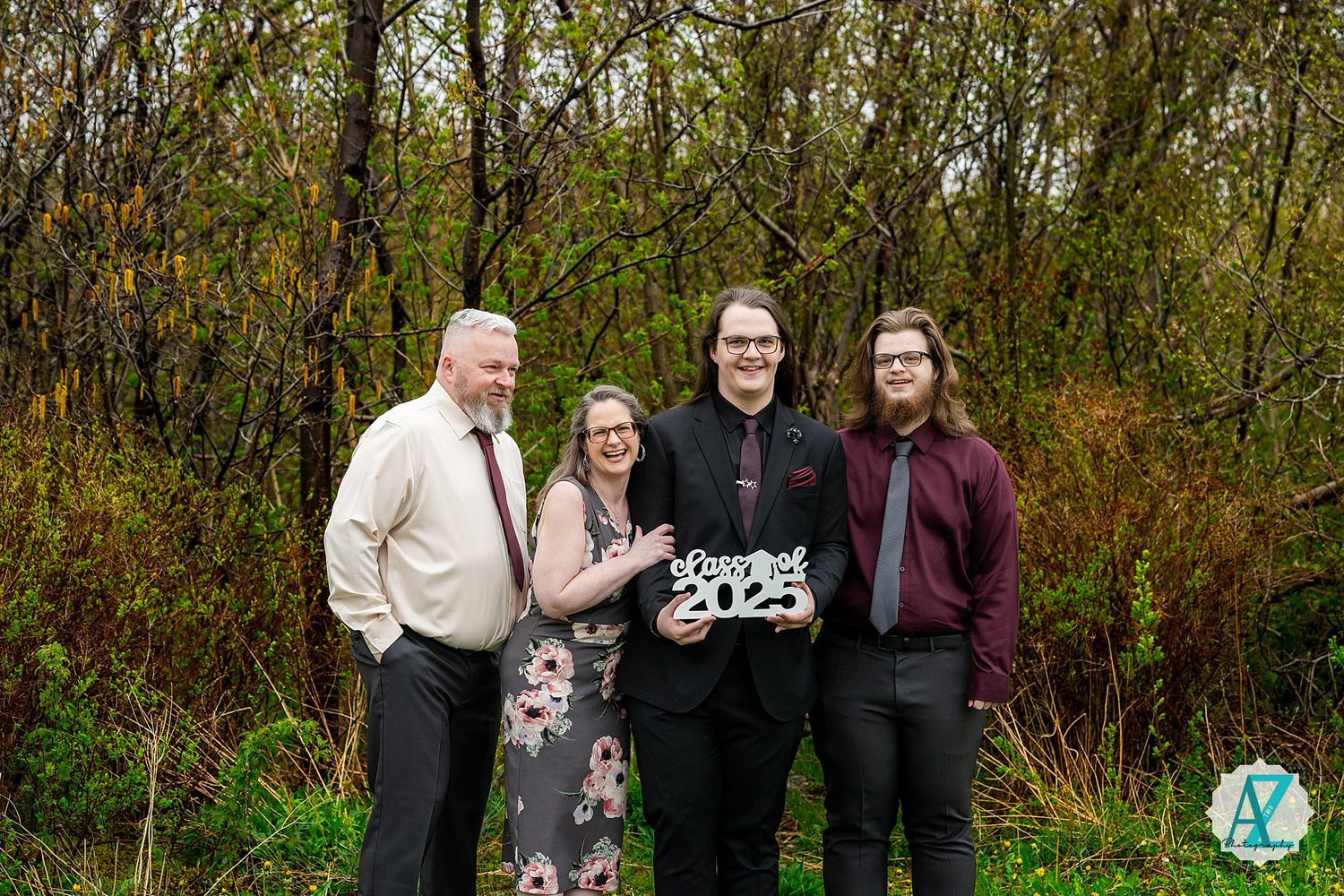 A group of people stand together outdoors in front of autumn foliage holding a festive sign.